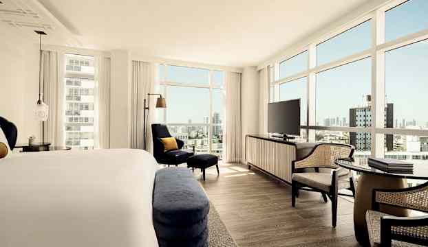 Hotellrum med säng, sittgrupp, en stor TV och stora fönster med utsikt över staden. (AI-genererad text)