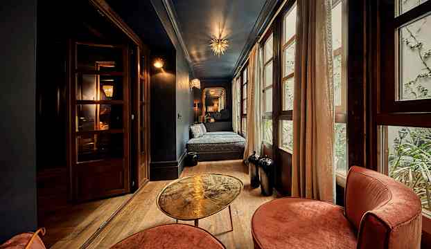 Ett sovrum med blå väggar, ett fönster med gardiner, en säng och en sittgrupp med bord. (AI-genererad text)