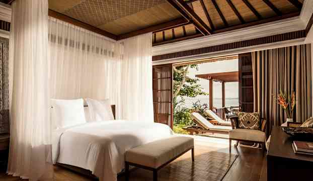 Välutrustat hotellrum med säng som har vita lakan och myggnät. Terrass med solstolar och utsikt mot havet. (AI-genererad text)