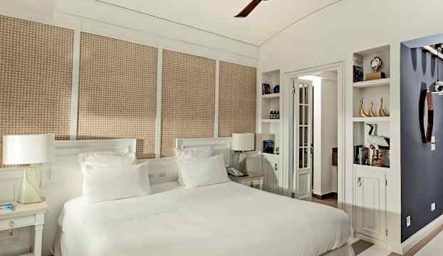 Ett sovrum med en dubbelsäng, ljusa sängkläder och inredning i vita och beige nyanser, samt en takfläkt. (AI-genererad text)