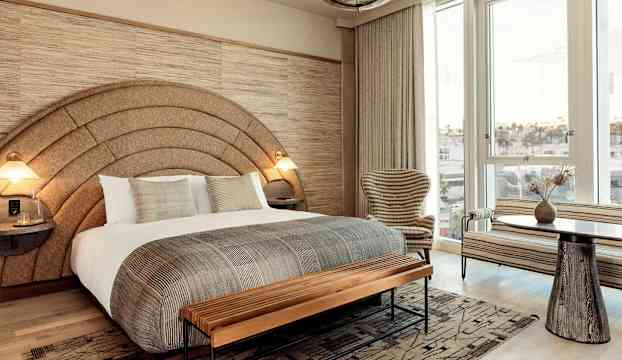 Ett sovrum med en stor säng, inrett i jordnära toner, inkluderar fönster med utsikt och moderna möbler. (AI-genererad text)