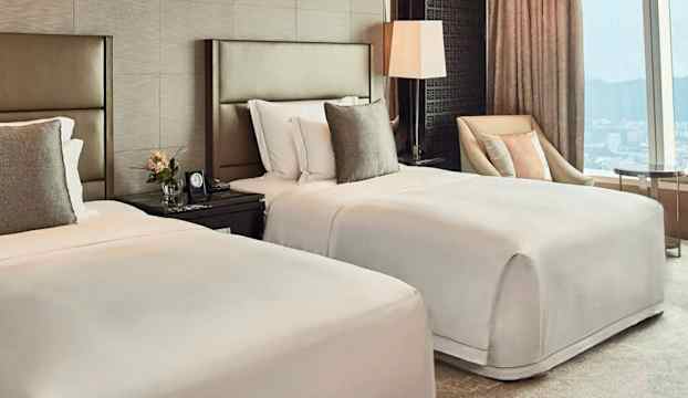 Ett hotellrum med två enkelsängar, nattduksbord, en fåtölj och ett stort fönster med utsikt. (AI-genererad text)