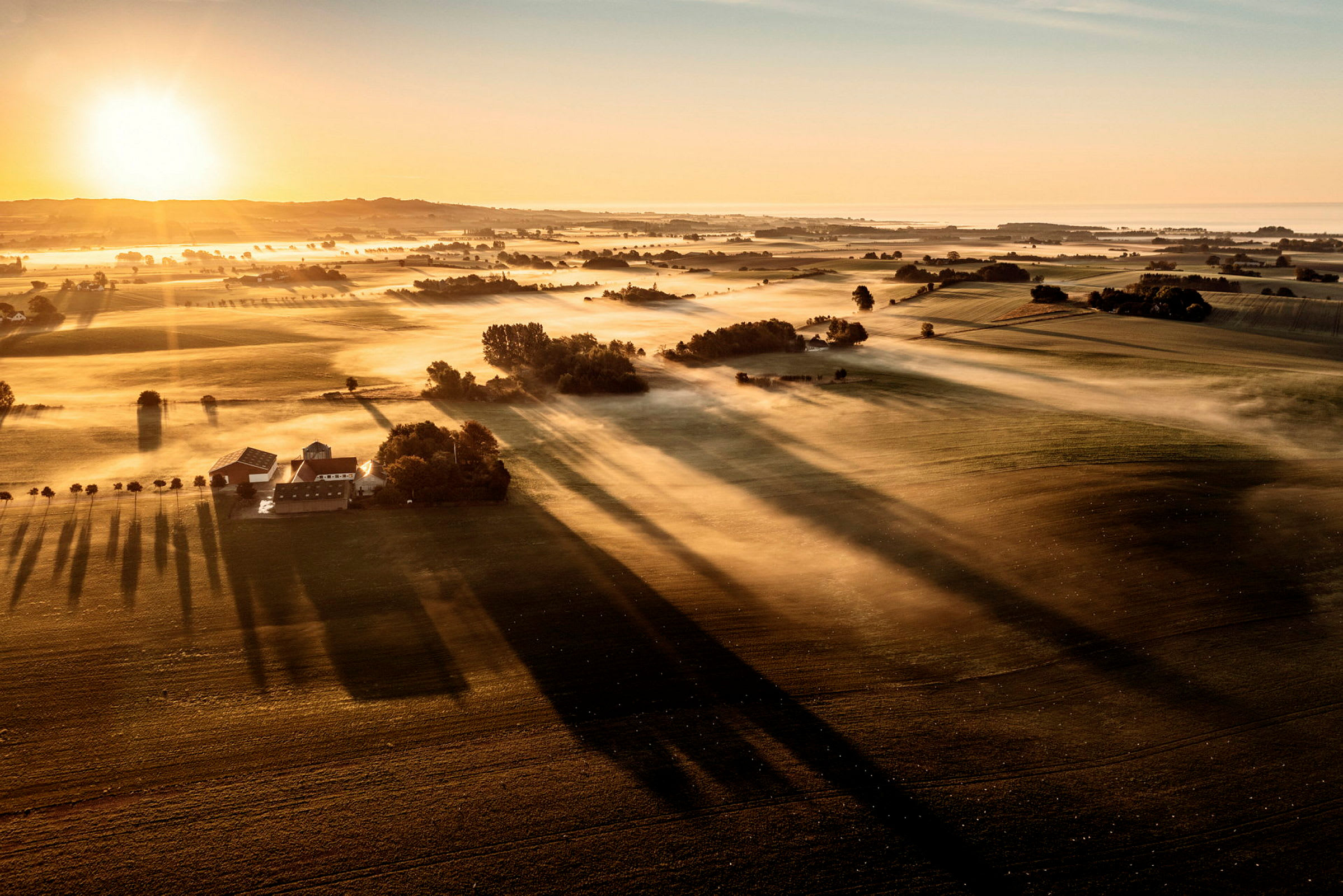 Flygfoto över ett landskap vid soluppgång med dimma över fälten. (AI-genererad text)