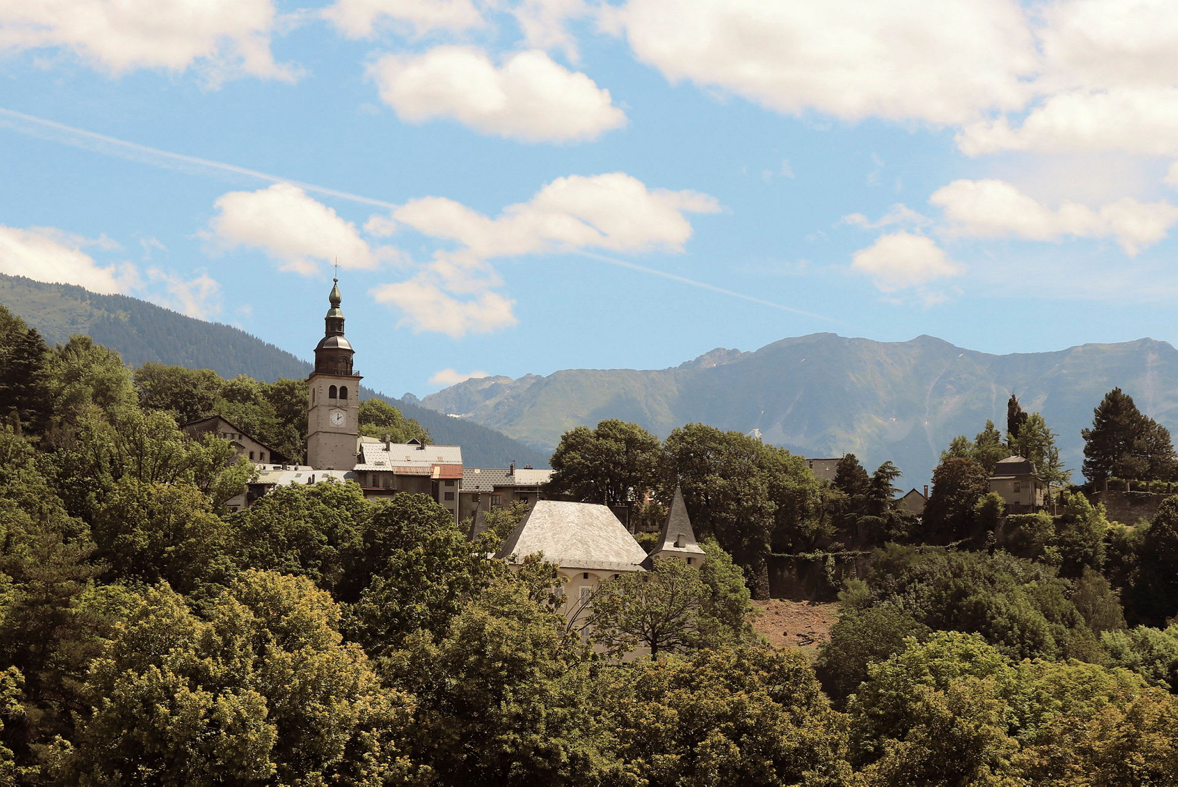 En kyrka och omgivande byggnader placerade i en skog med berg i bakgrunden. (AI-genererad text)