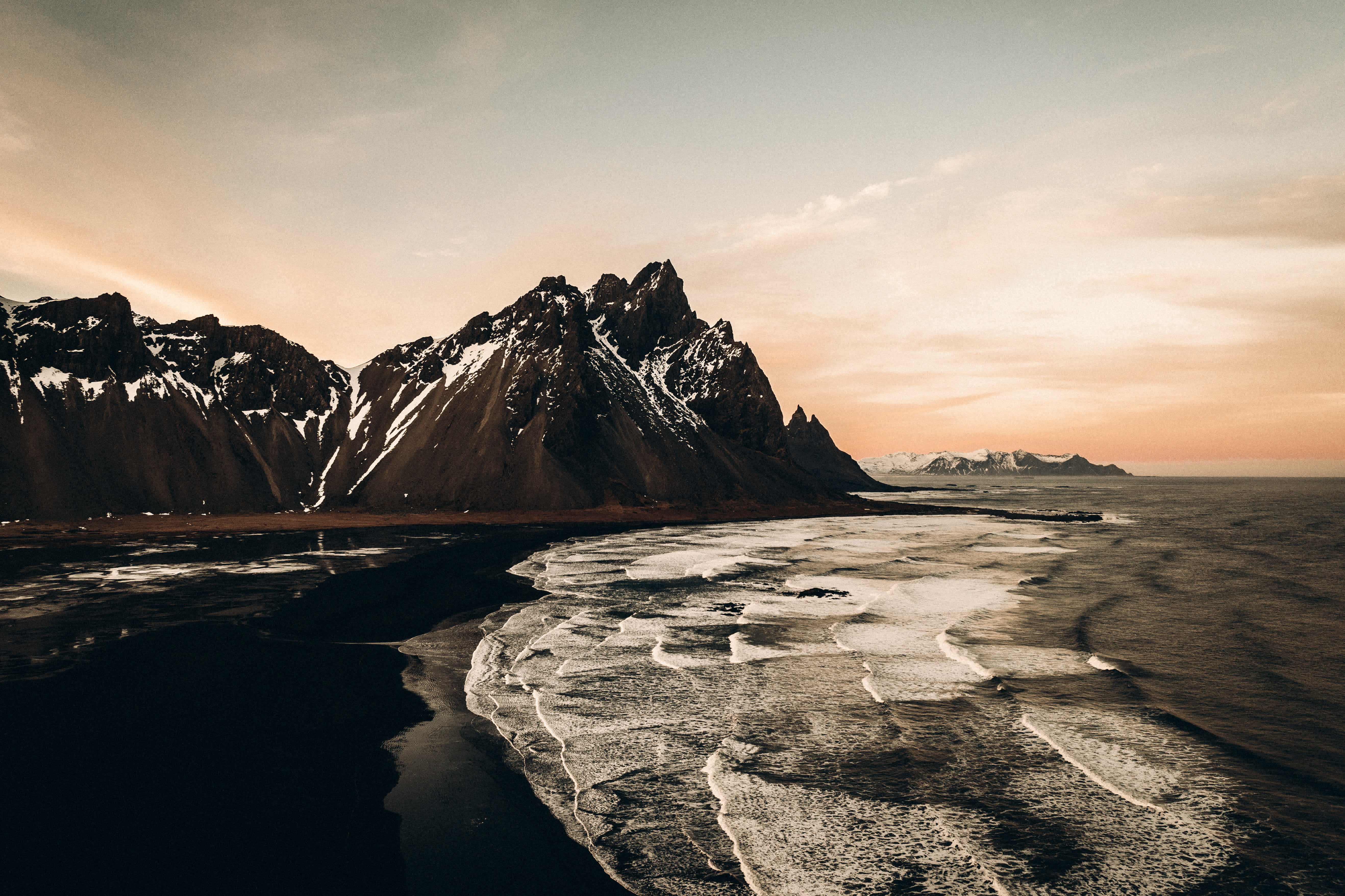 Kust med vågor och berg med snö under solnedgång. (AI-genererad text)