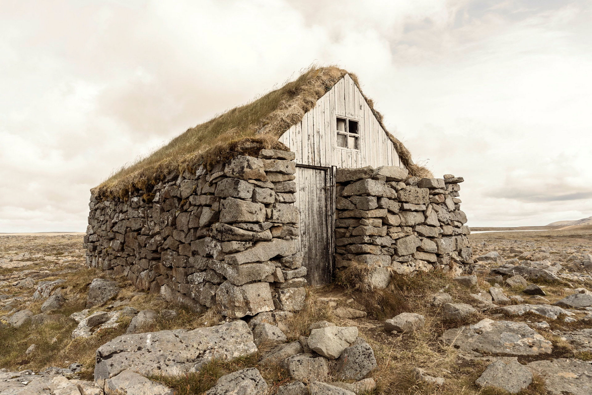 Ett hus med torvtak och stenmur, beläget i öppen terräng. (AI-genererad text)