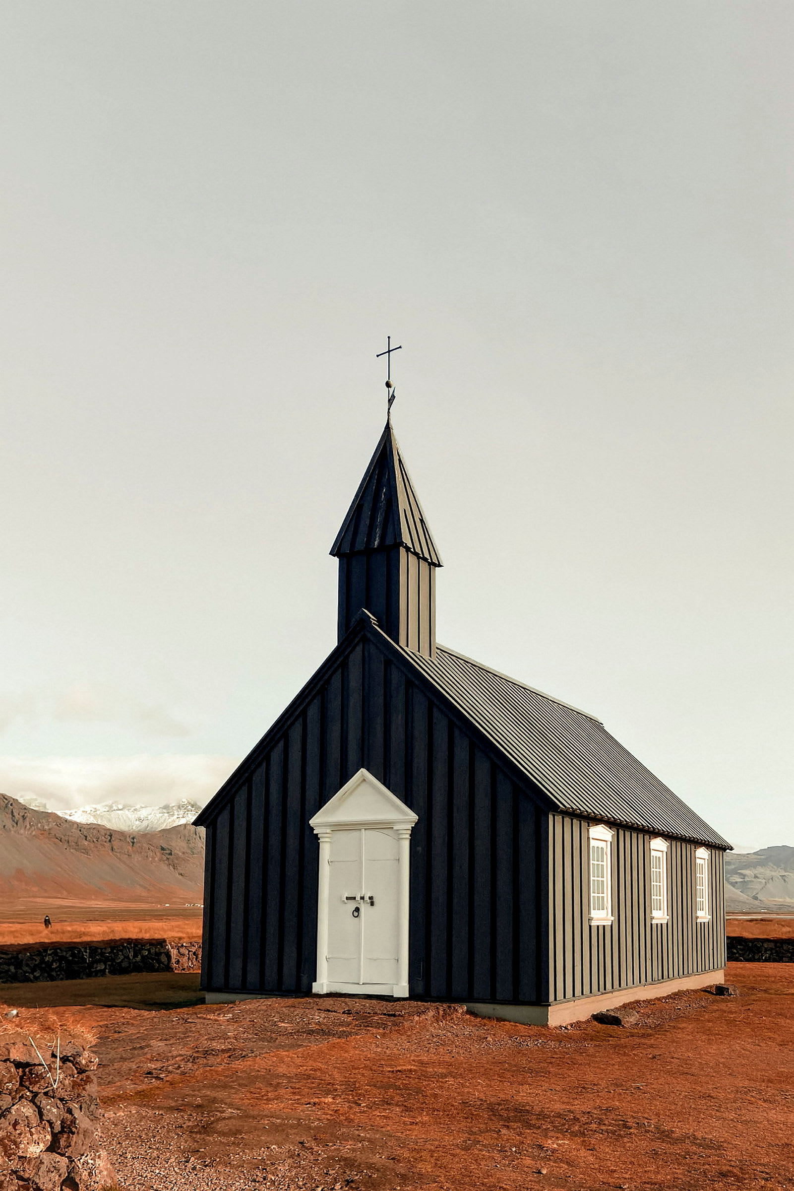 En liten svart träkyrka med ett vitt kors på taket, placerad i ett öde landskap. (AI-genererad text)