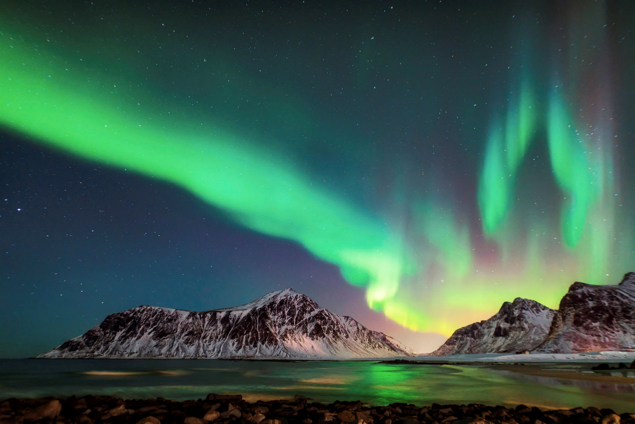 Nordljus över ett snötäckt bergslandskap och en stilla kust. (AI-genererad text)