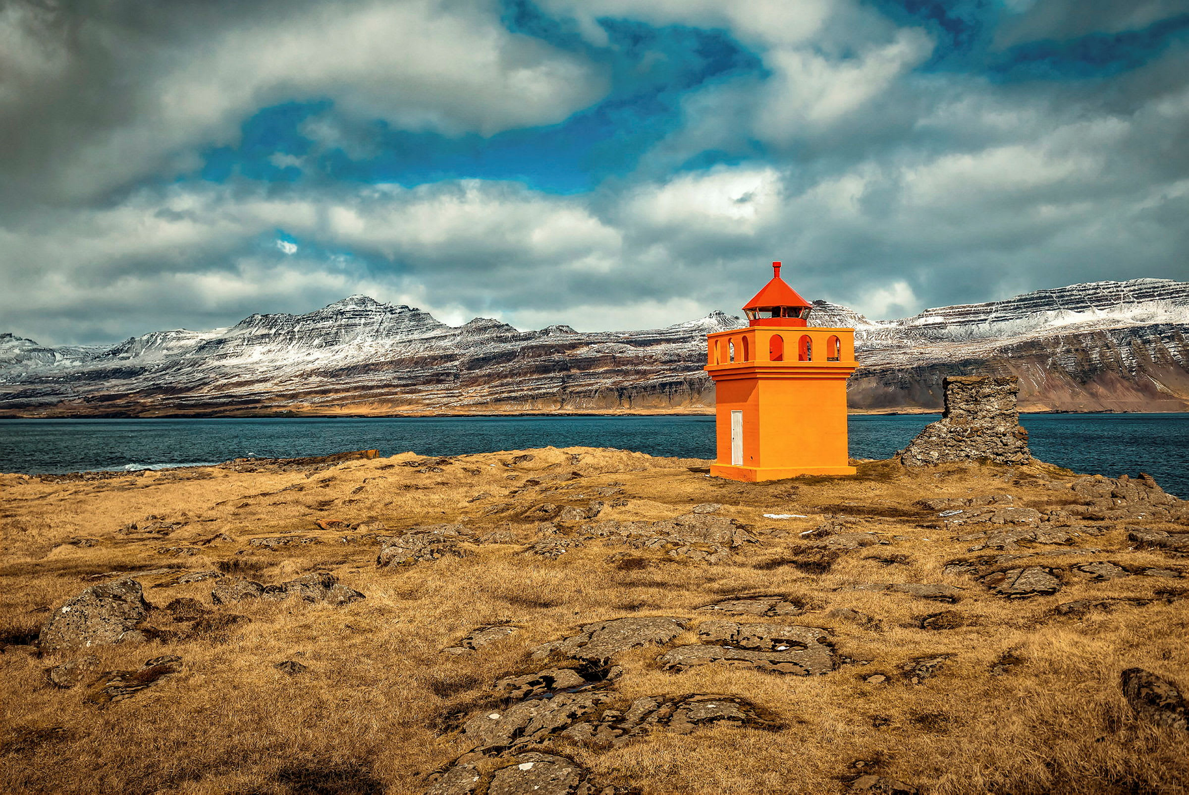 Orange fyr bredvid en ruin, med berg och hav i bakgrunden. (AI-genererad text)