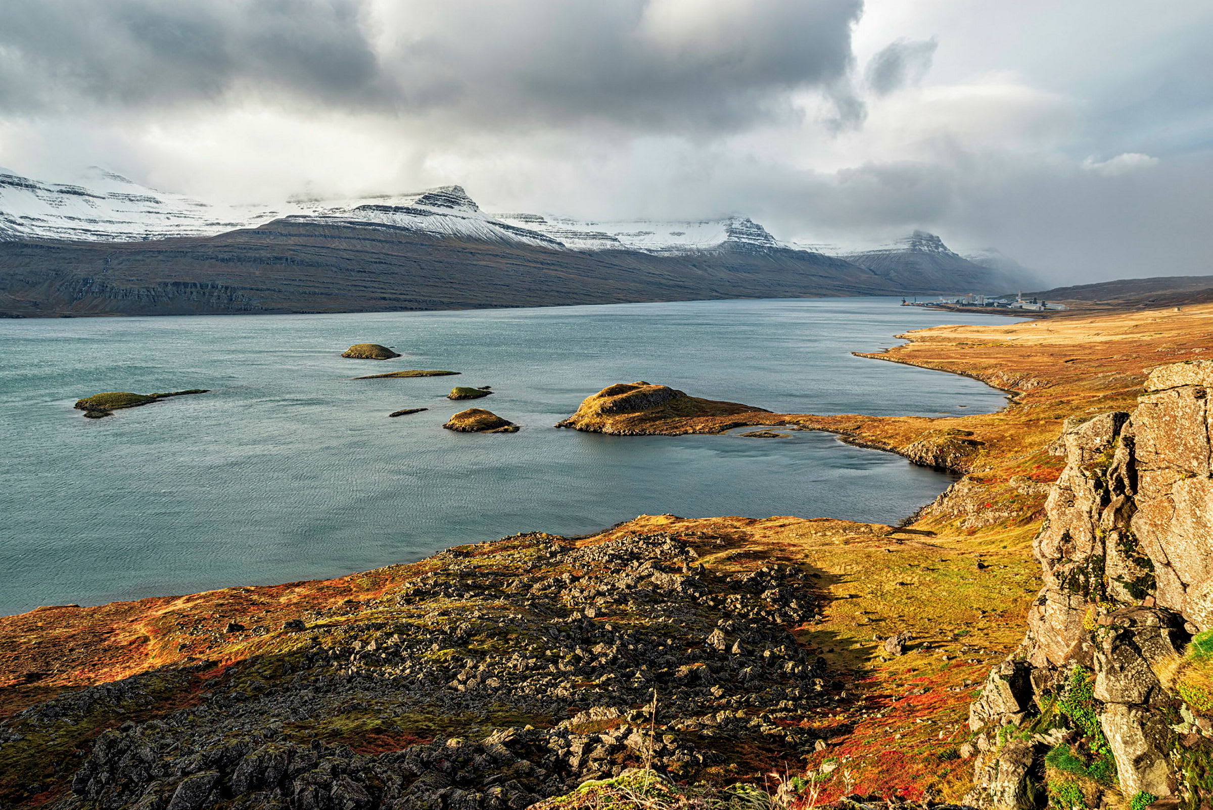 Landskap med klippor, havsvik och snötäckta berg i bakgrunden. (AI-genererad text)