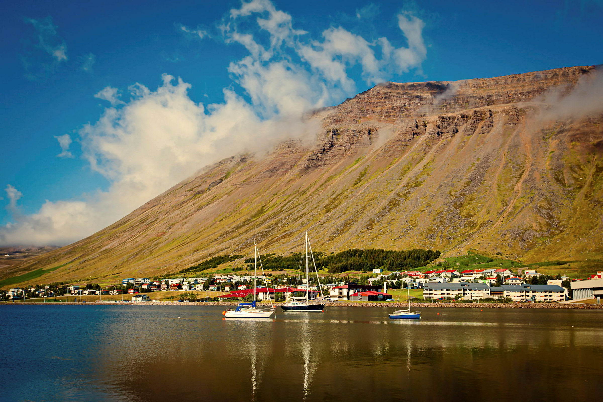 Vy över en fjord med segelbåtar och en by framför ett berg. (AI-genererad text)