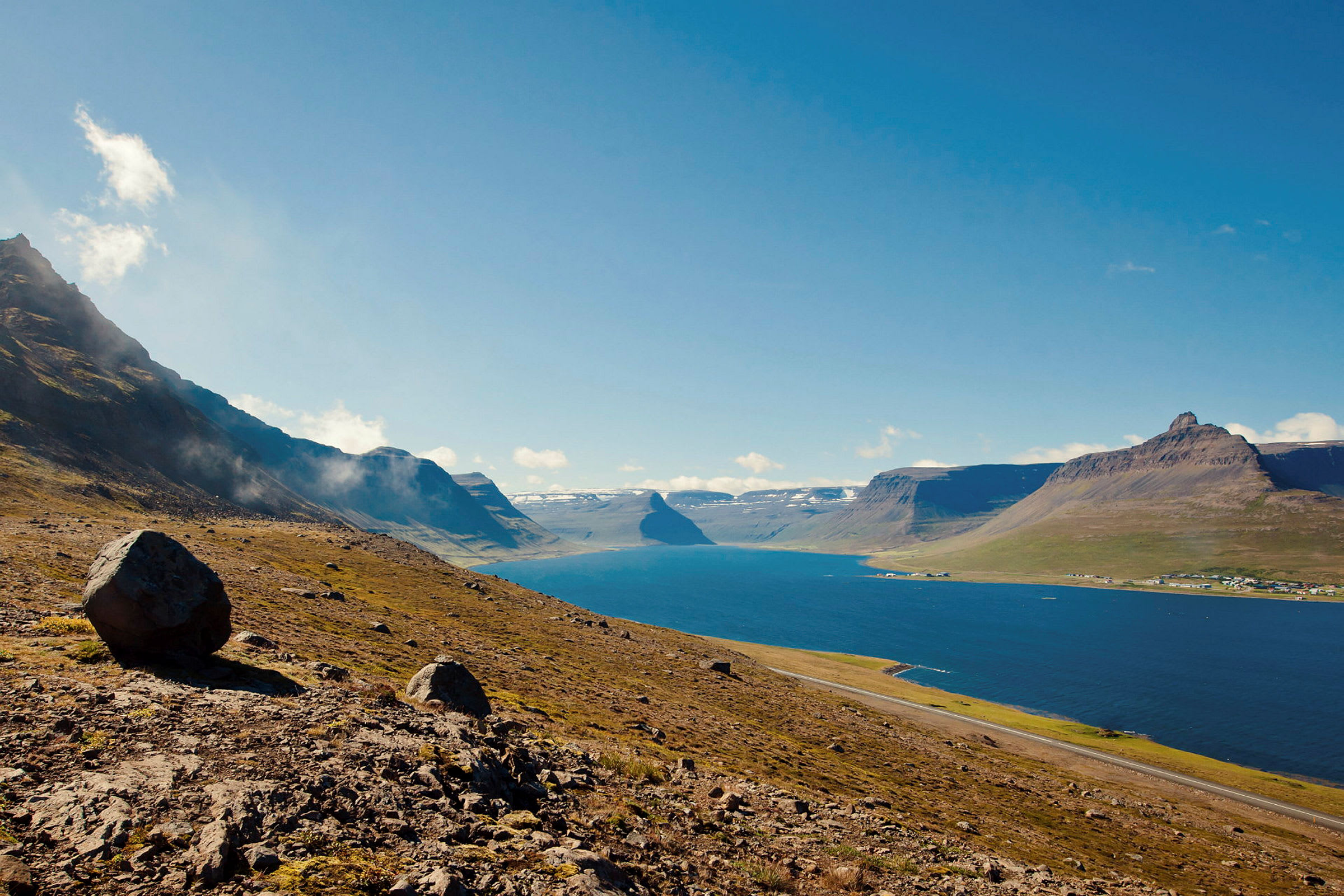 Bergsluttning vid en blå fjord under klar himmel. (AI-genererad text)