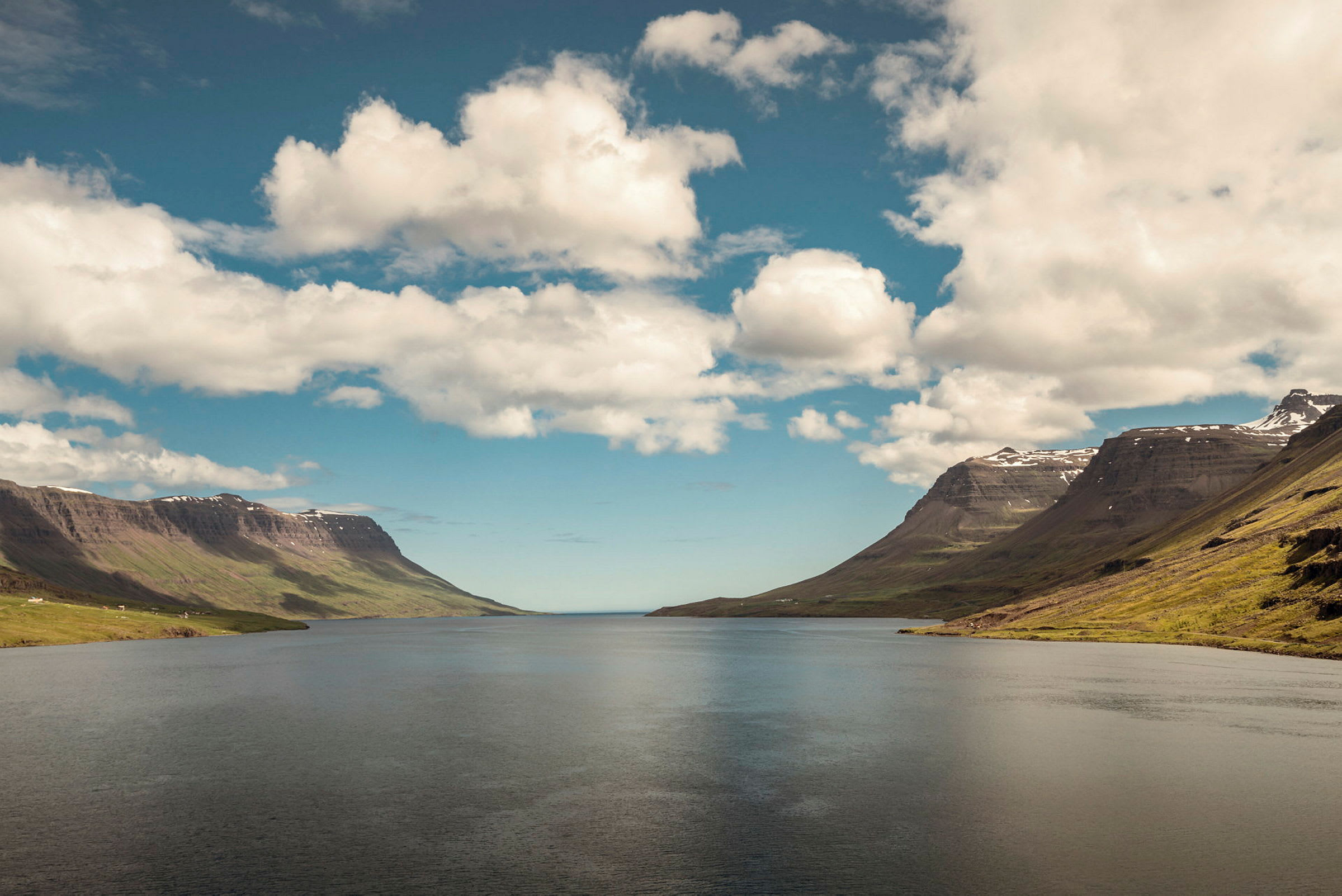 Fjordlandskap med berg på båda sidor under en blå himmel med moln. (AI-genererad text)