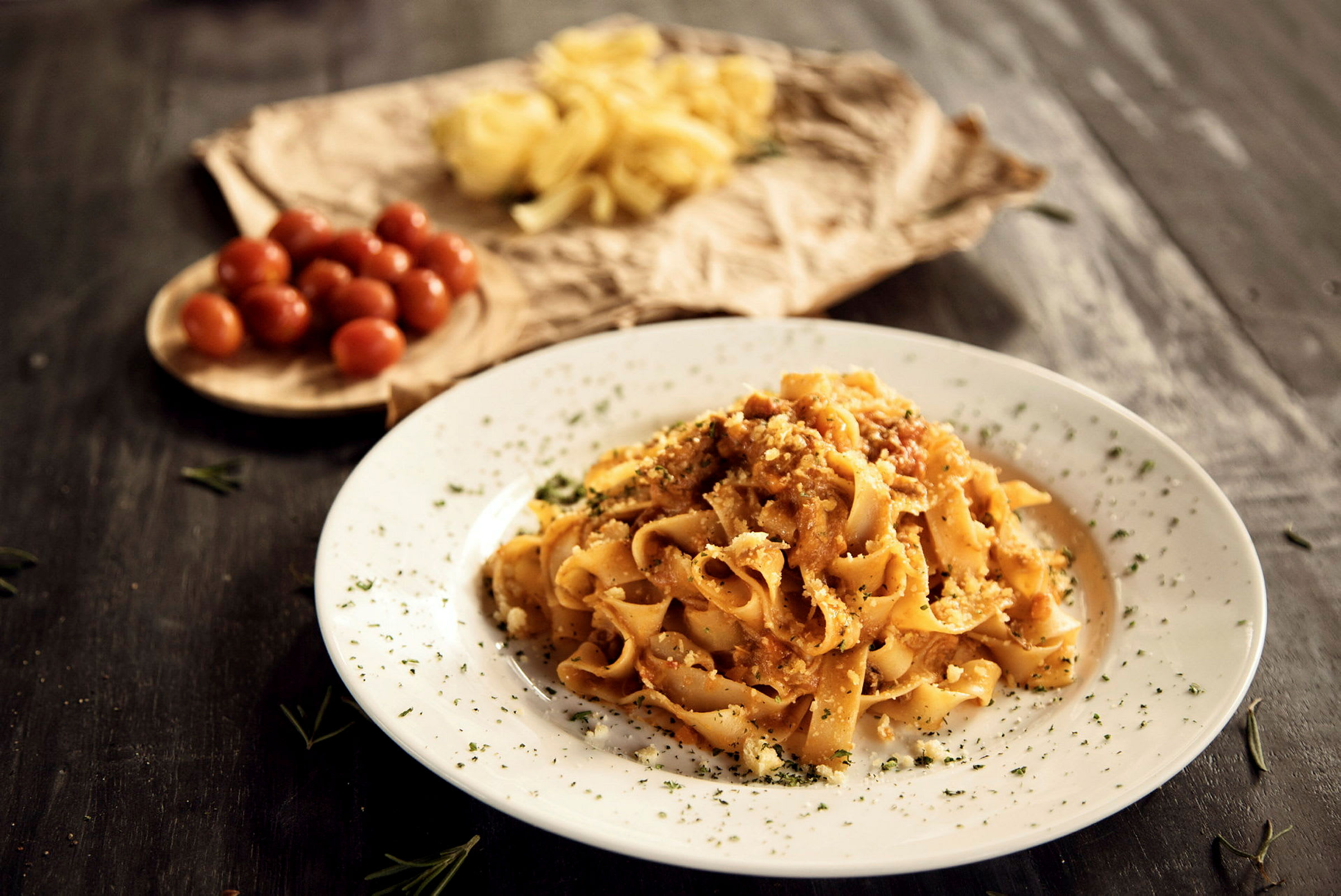 En tallrik med pasta toppad med sås och örter, med körsbärstomater och rå pasta i bakgrunden. (AI-genererad text)