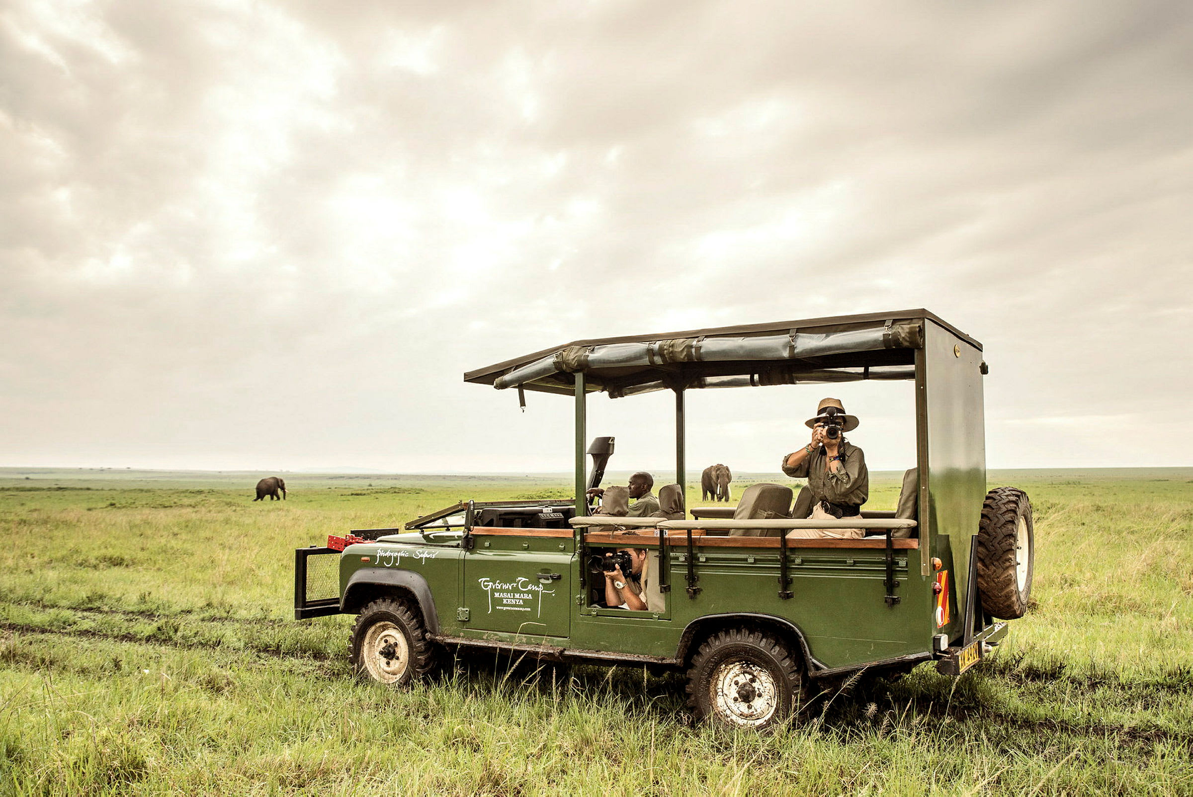 En grön safari-jeep på en grässlätt med i bakgrunden en elefant. (AI-genererad text)