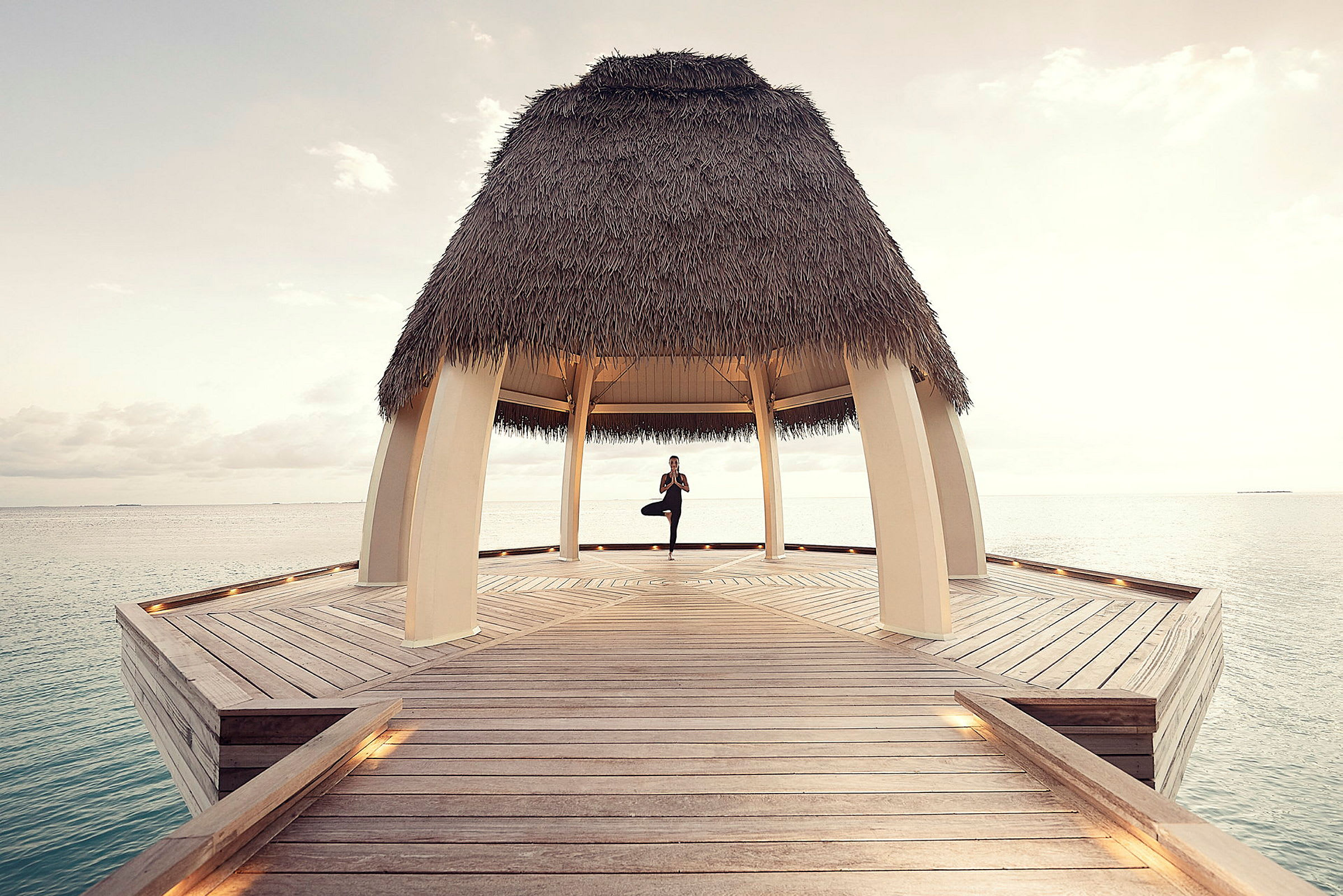 Person som utför yoga under en halmtäckt paviljong på en brygga vid havet. (AI-genererad text)