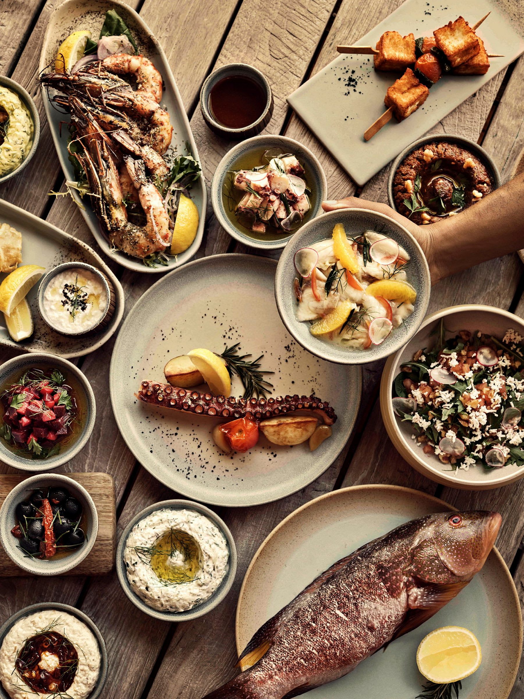 Ett bord med olika tallrikar och skålar fyllda med delikatesser som fisk, skaldjur, sallad och dip. (AI-genererad text)