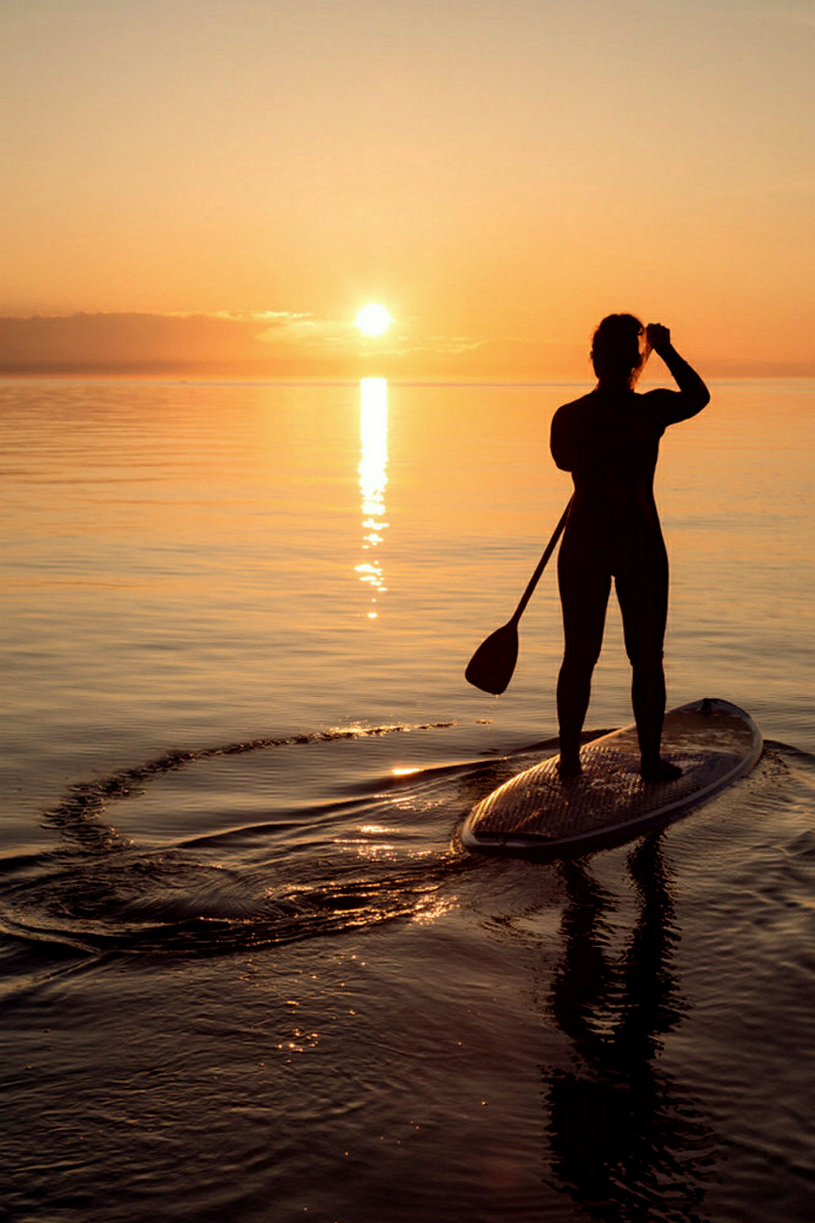 Silhuetten av en person på en paddleboard vid solnedgången. (AI-genererad text)
