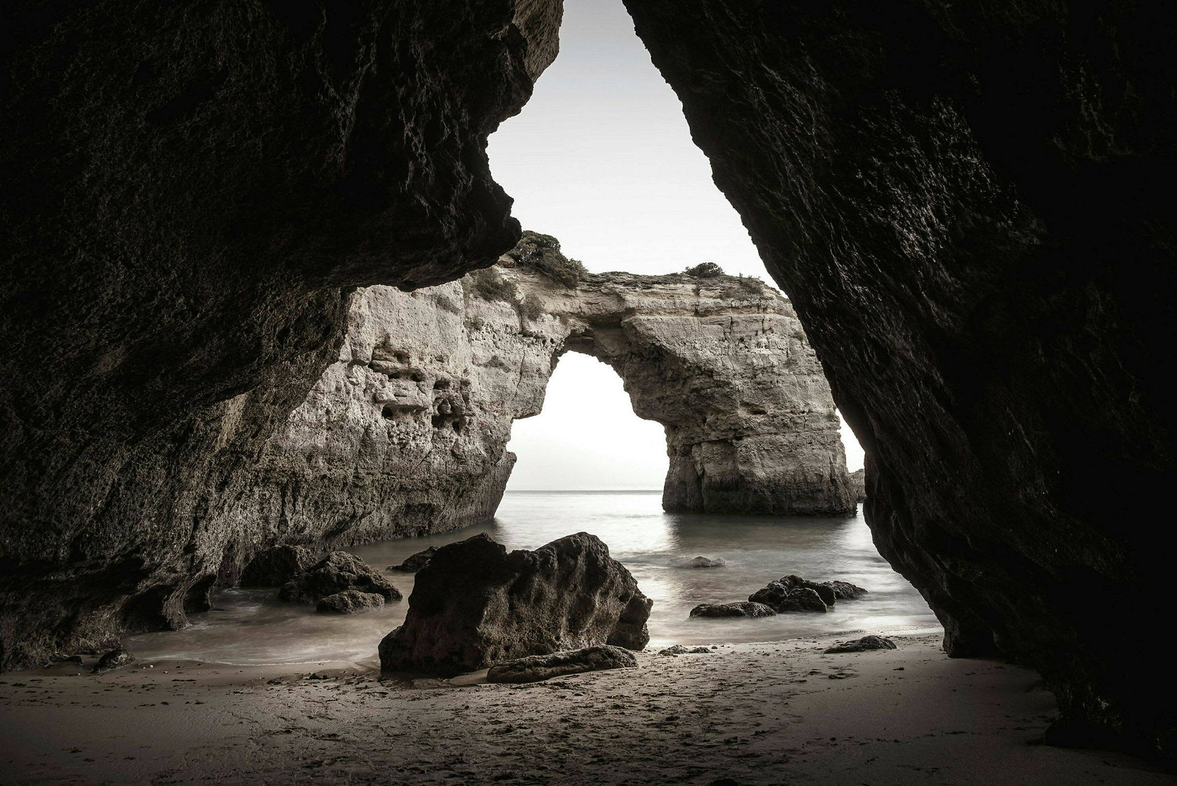 Utsikt från insidan av en grotta mot en naturlig stenbåge vid havet. (AI-genererad text)