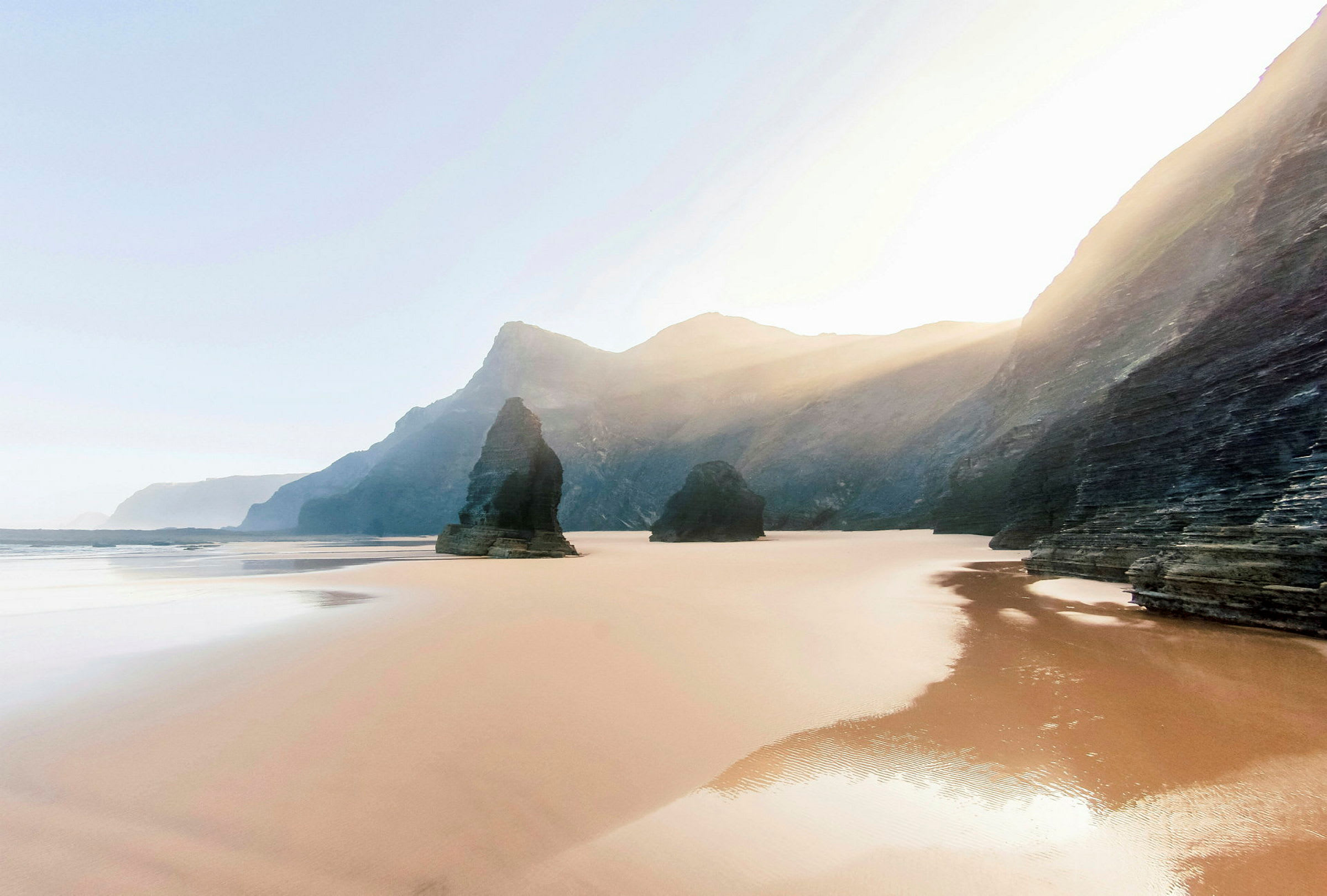 Sandstrand med klippformationer och berg i bakgrunden. (AI-genererad text)