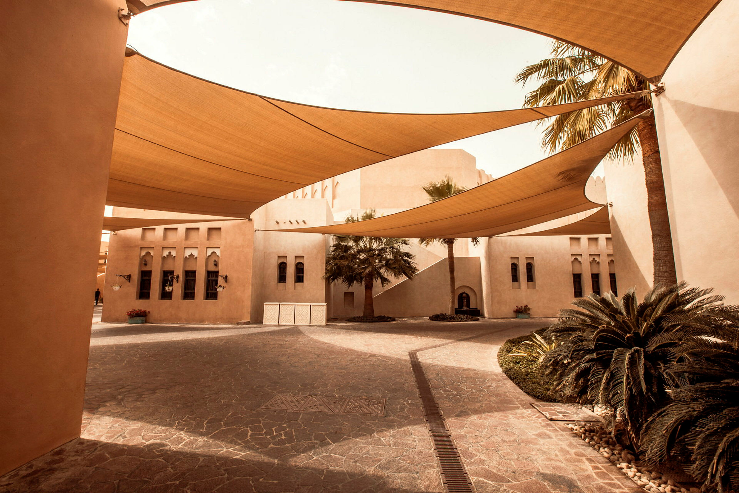 Arabiskt byggnadskomplex med tältliknande solskydd och palmer. (AI-genererad text)