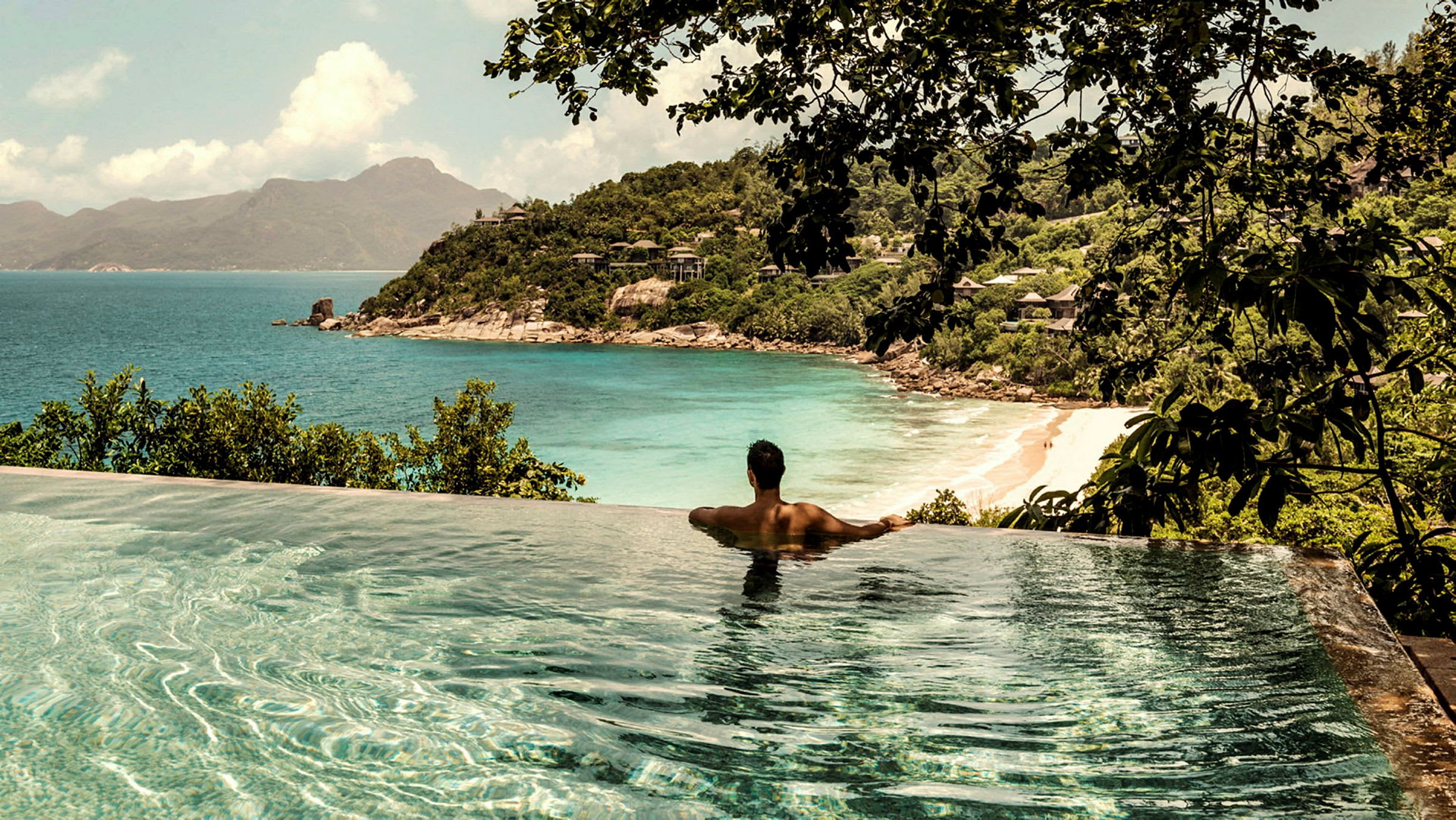 En person sitter vid kanten av en pool med utsikt över en strand och havet. (AI-genererad text)