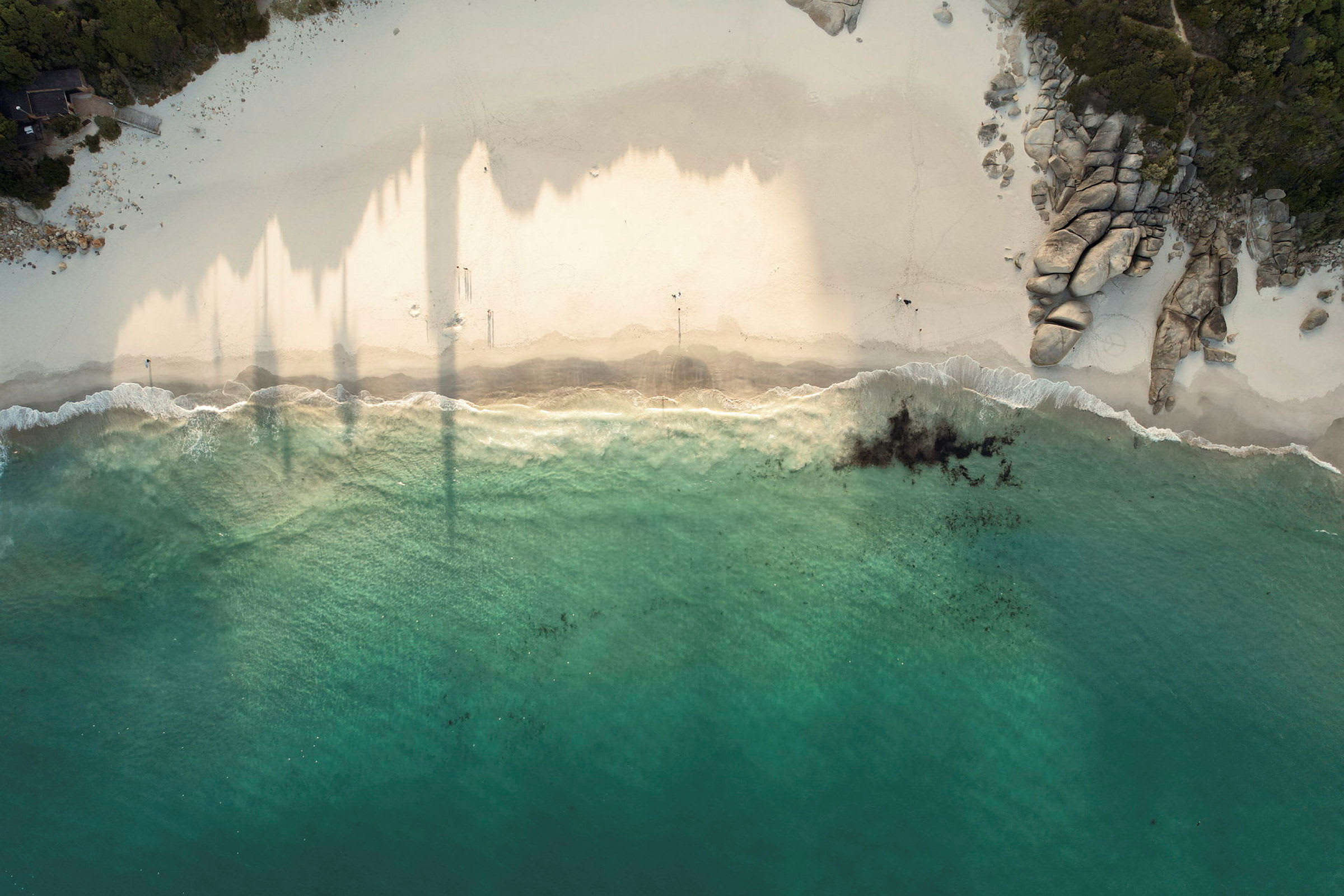 Flygfoto av en strand med klart vatten, sand och klippor. (AI-genererad text)