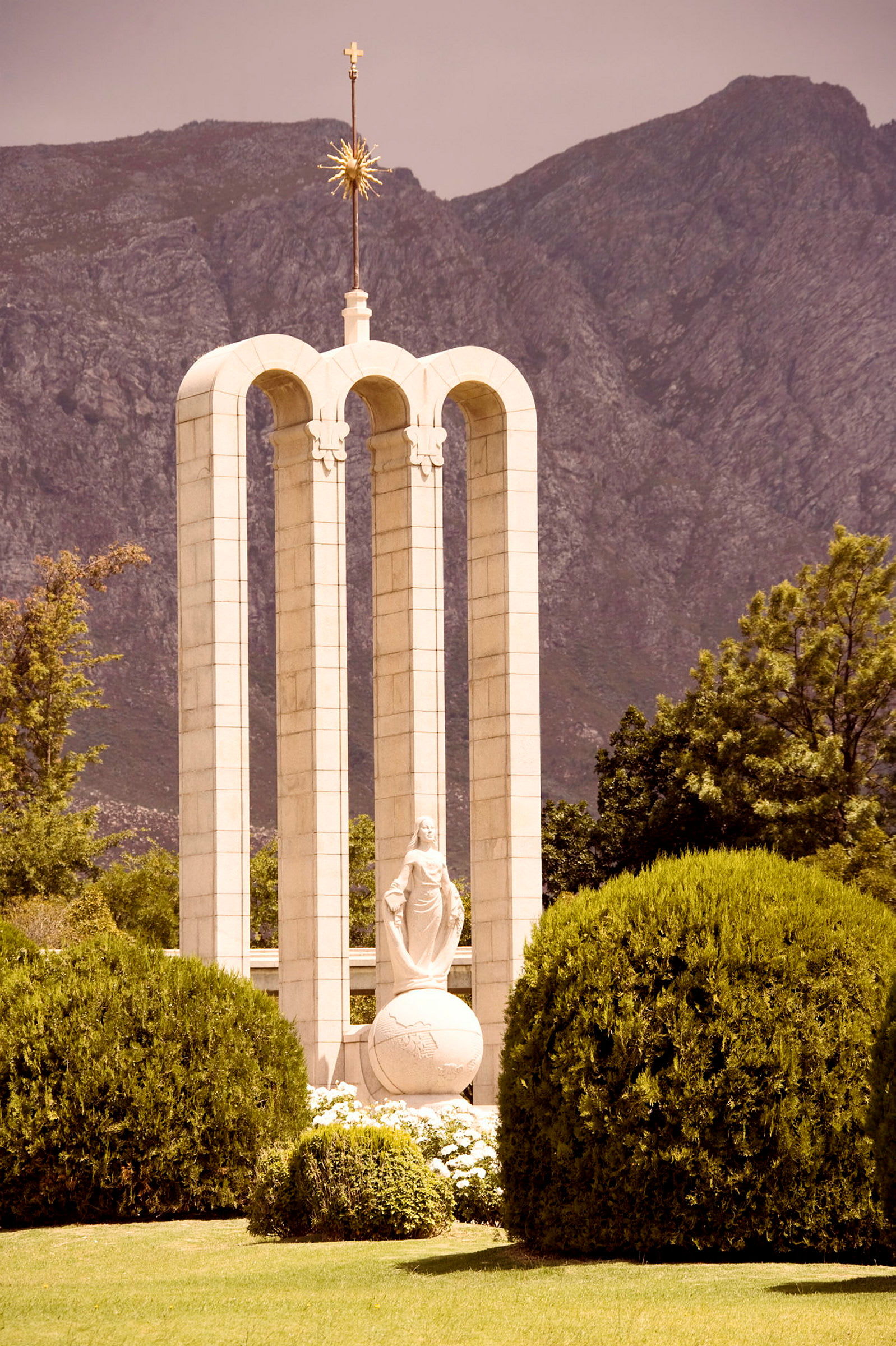 Stenmonument med valv, en skulptur och berg i bakgrunden. (AI-genererad text)