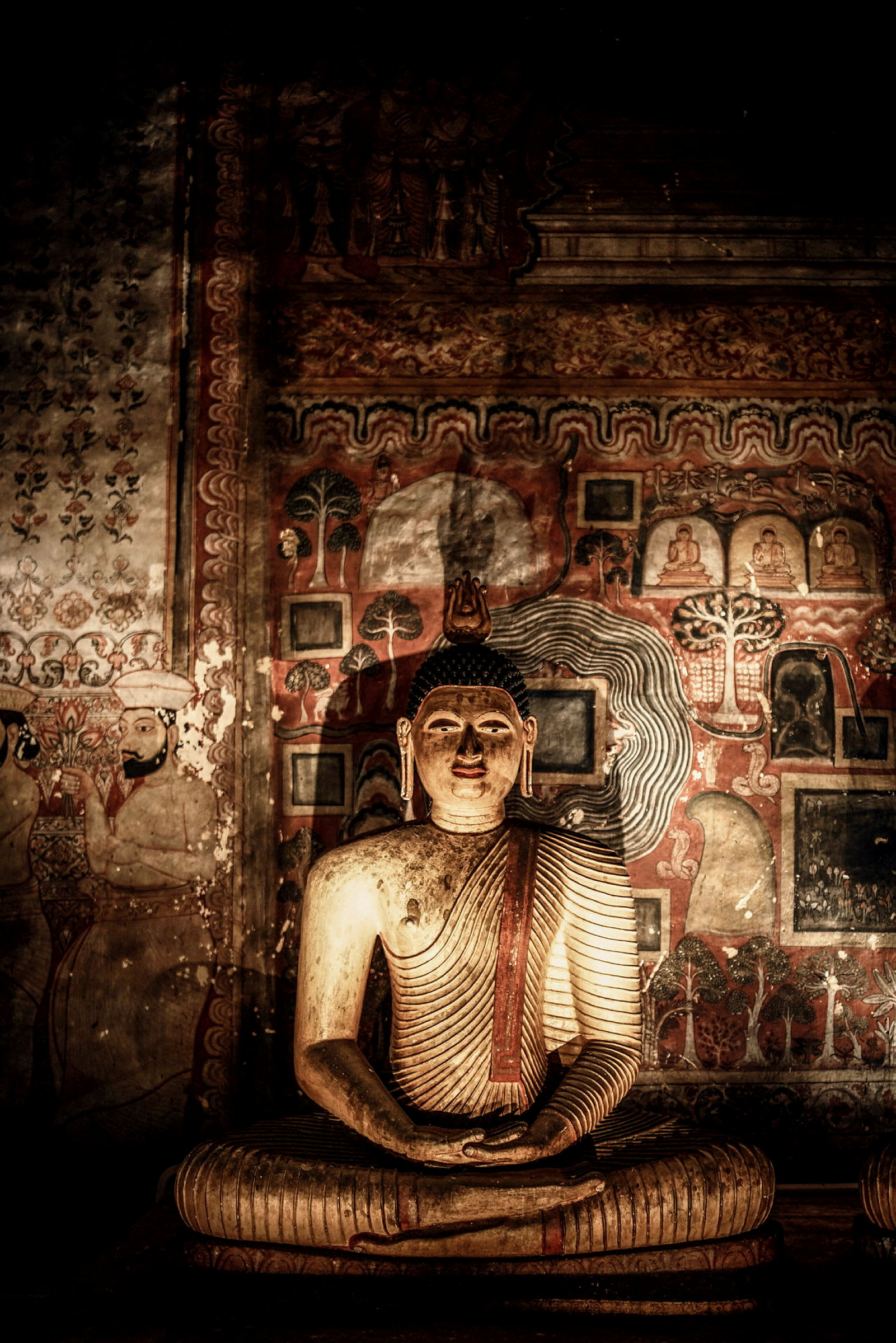 En gyllene Buddha-staty framför detaljerade väggmålningar i varma toner. (AI-genererad text)