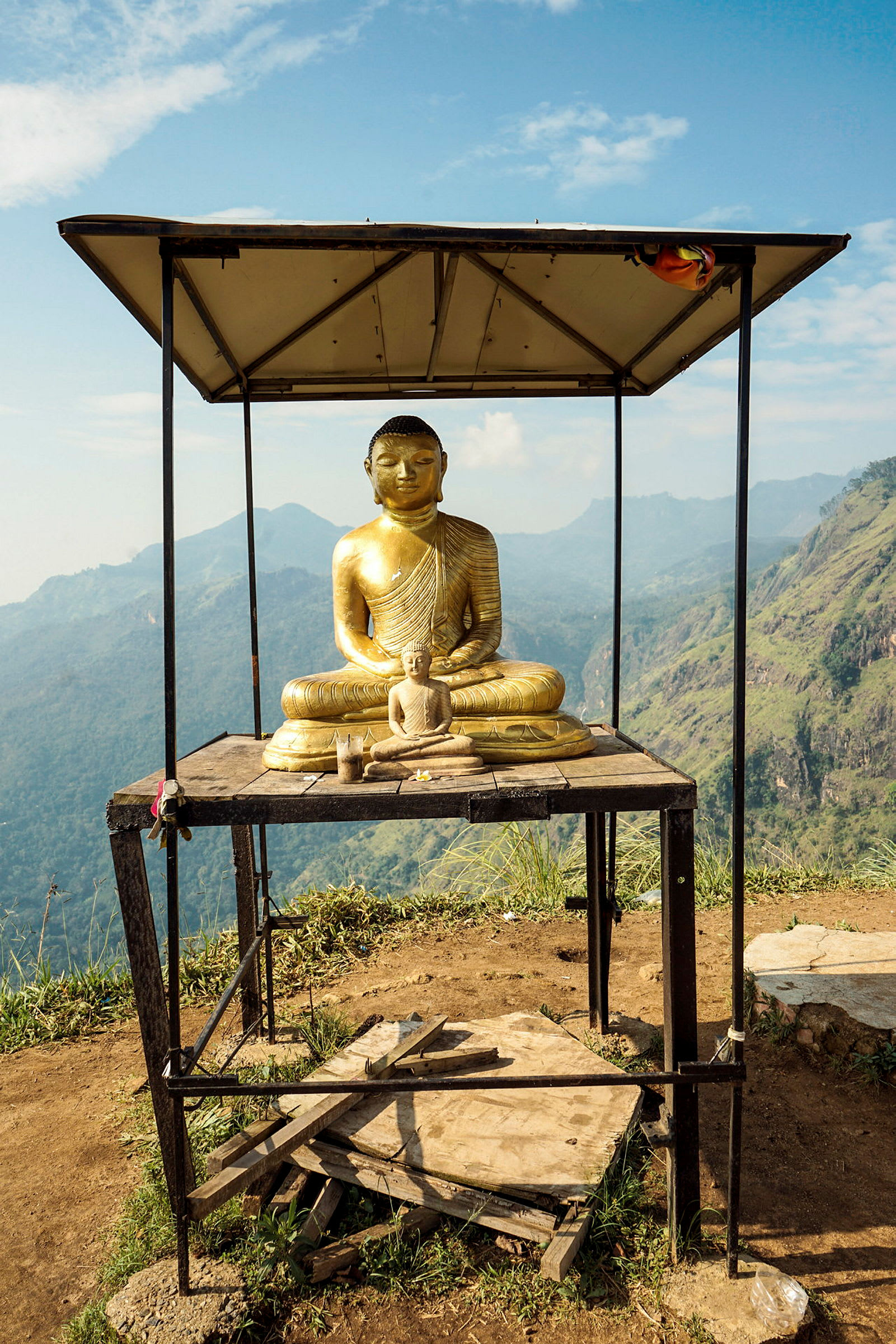 Staty av en sittande Buddha under ett skydd där den omgivande naturen med berg kan ses. (AI-genererad text)