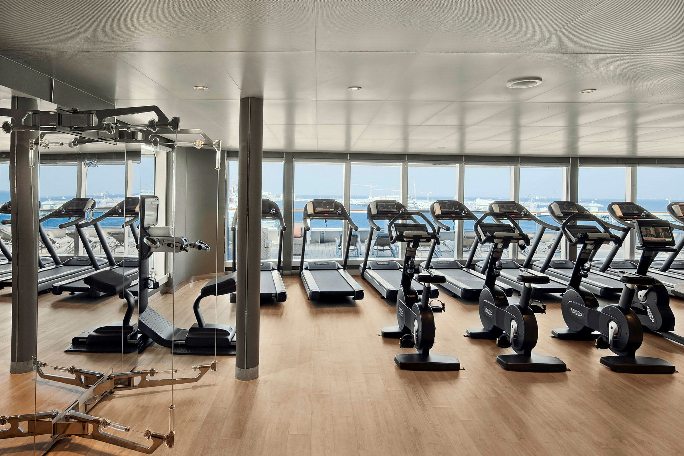Ett gym med träningsutrustning, inklusive löpband och motionscyklar, med utsikt över havet. (AI-genererad text)