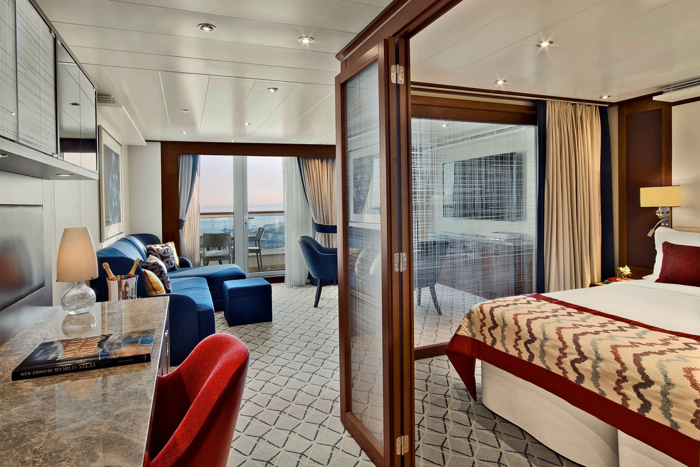 Ett hotellrum med sittgrupp, skrivbord och säng, samt balkong med utsikt. (AI-genererad text)