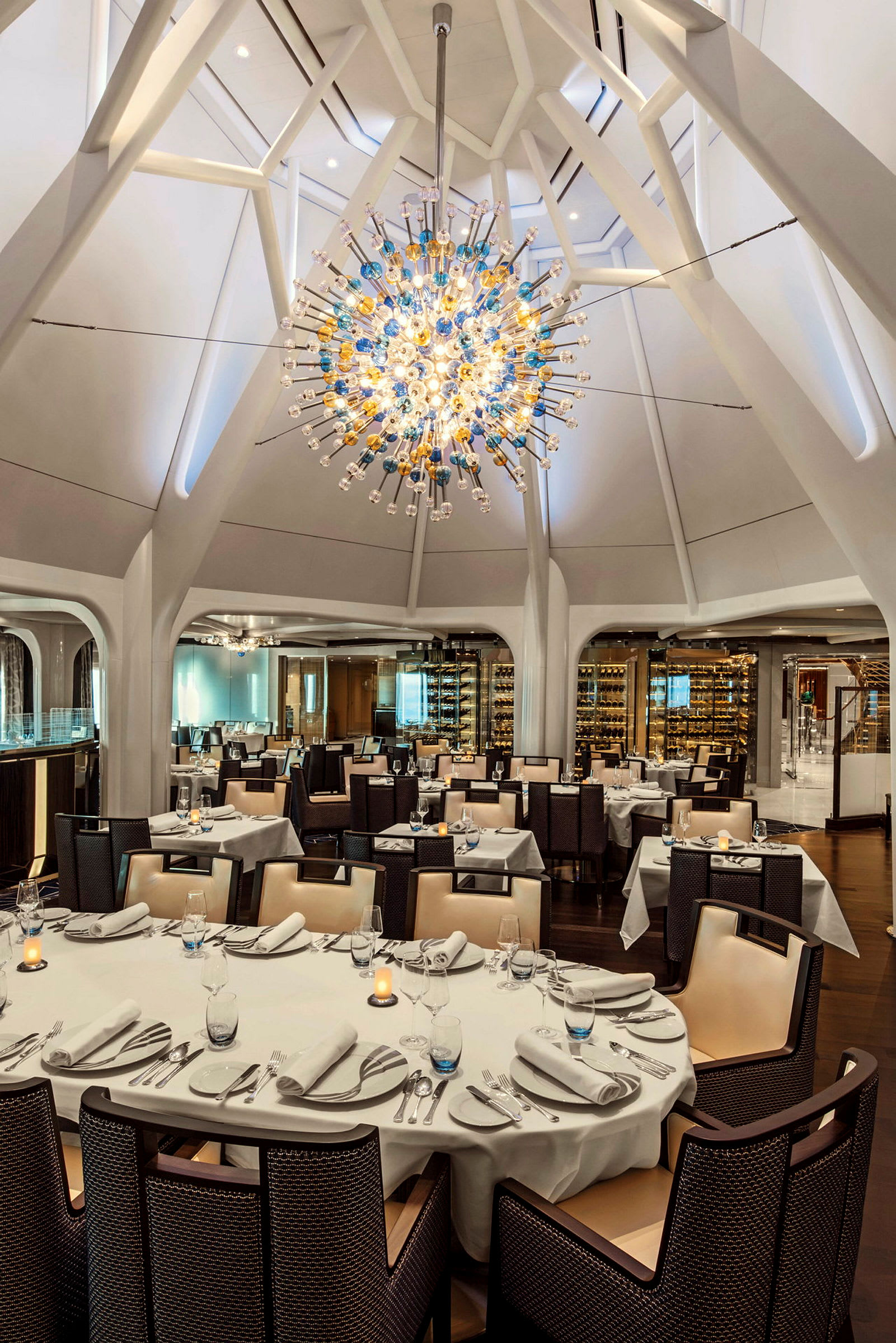En elegant restaurang med dukade bord och en stor, färgglad hängande ljuskrona i taket. (AI-genererad text)