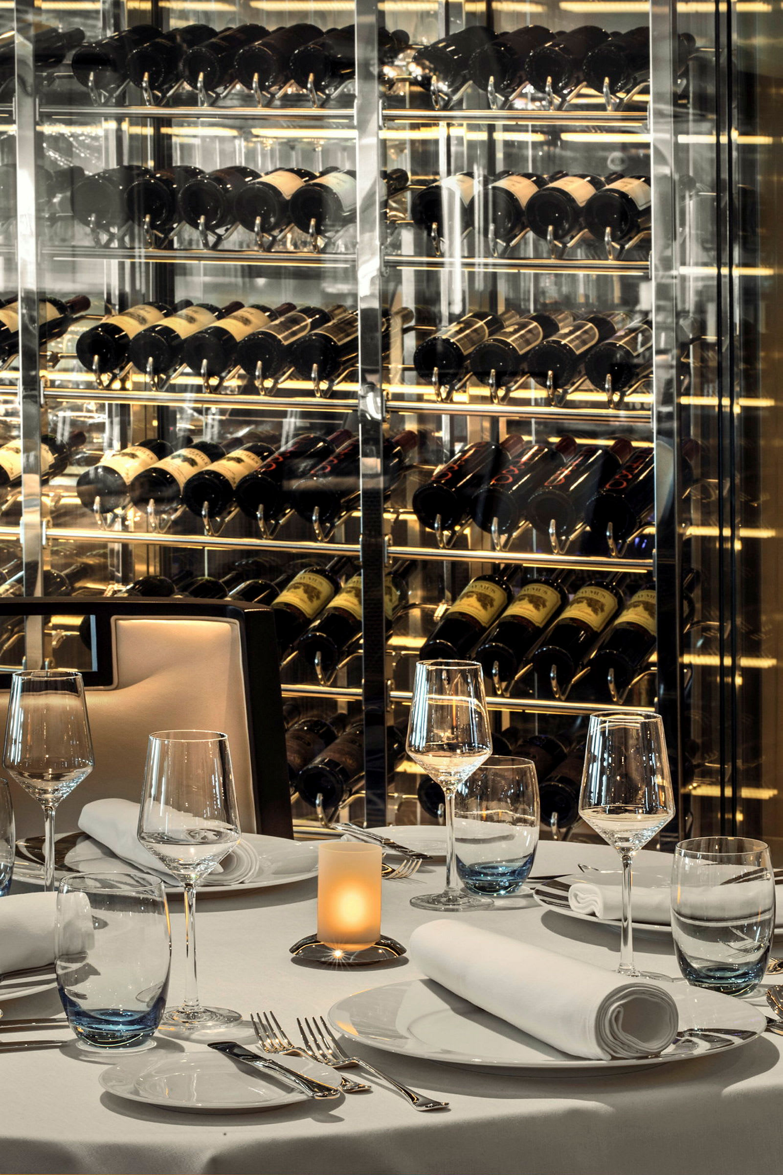 En elegant dukad restaurang med vinglas, bord och en vägg med vinkällarförvaring i bakgrunden. (AI-genererad text)