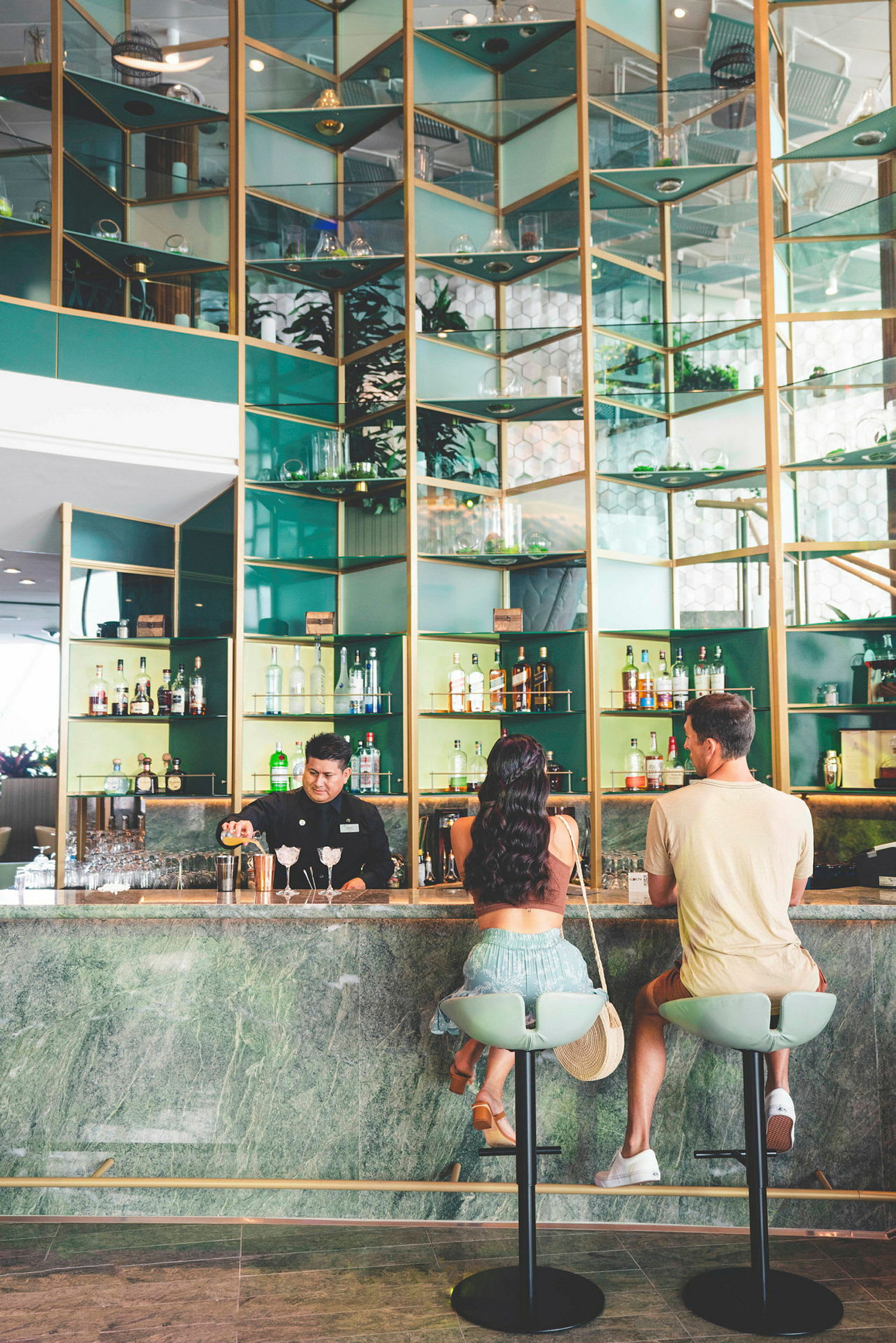 En bar med gröna och gyllene detaljer, där två personer sitter på barstolar och en person står bakom baren. (AI-genererad text)