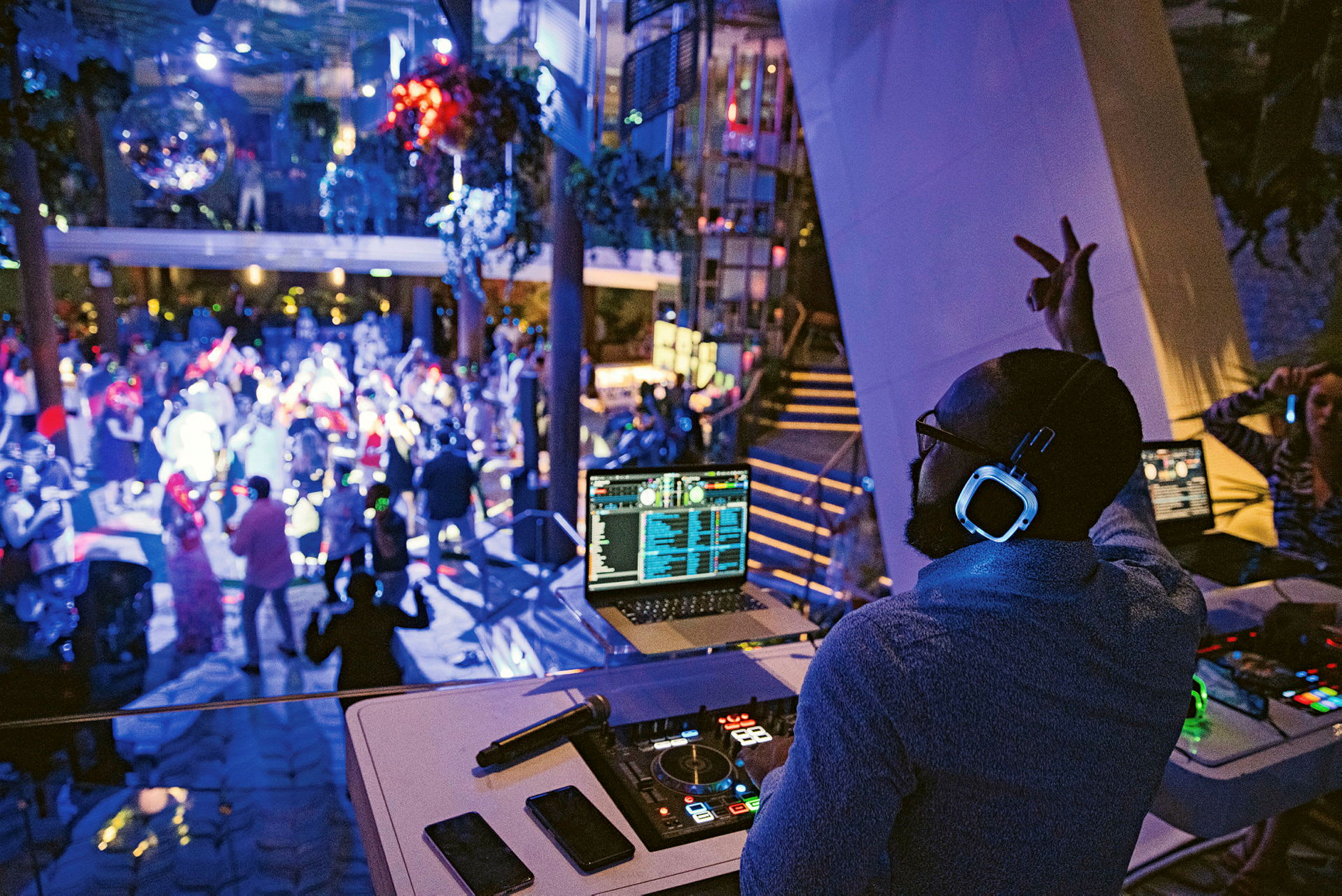 En DJ står vid sitt mixerbord och spelar musik på en nattklubb där människor dansar under blinkande ljus. (AI-genererad text)