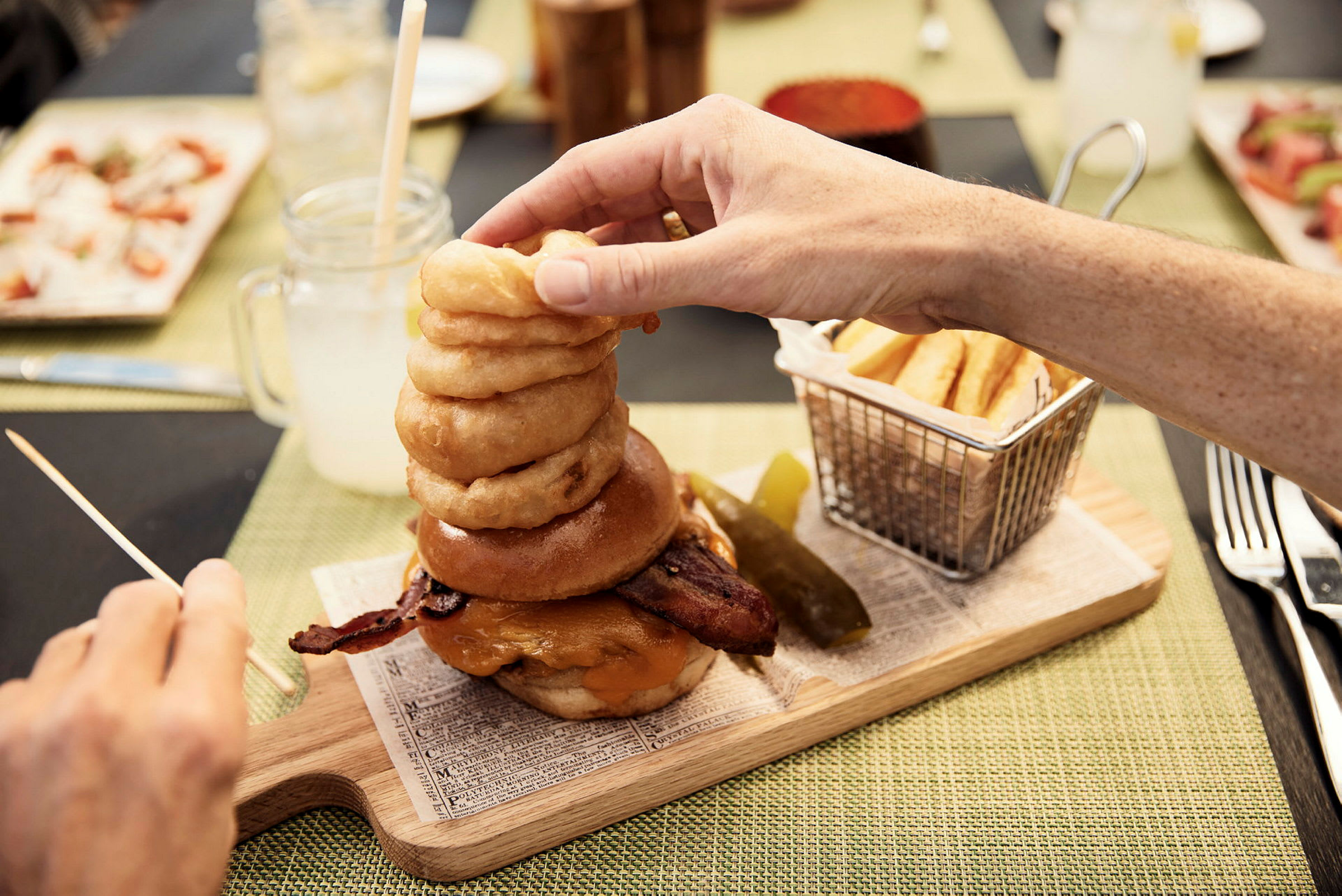 En hamburgare med bacon, ost och lökringar, serverad med pommes frites och en gurkskiva. (AI-genererad text)