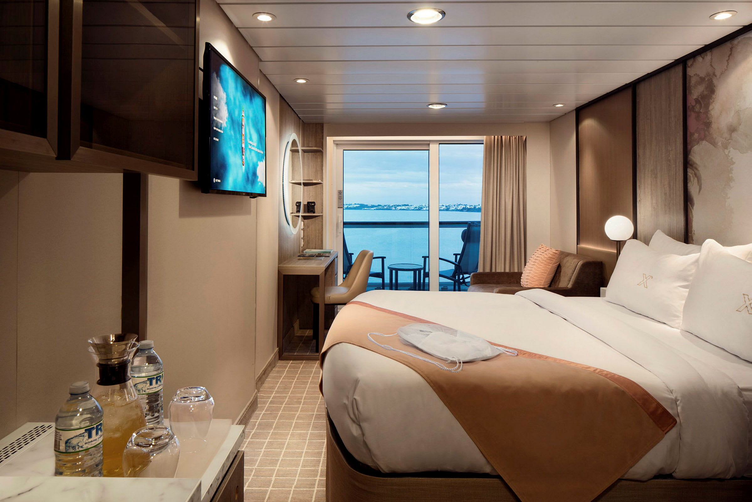 Hotellrum med en dubbelsäng, sittplats, arbetsbord och utsikt över havet från en balkong. (AI-genererad text)