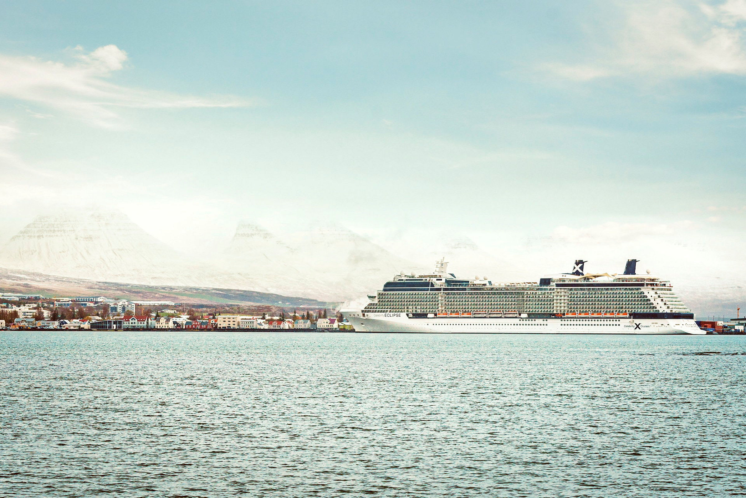 Kryssningsfartyg vid hamn, stad och berg i bakgrunden. (AI-genererad text)