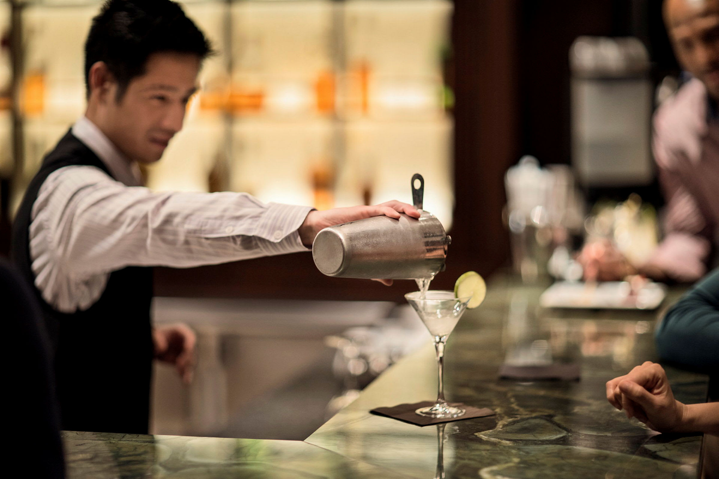 En server som häller en drink i ett cocktailglas. (AI-genererad text)