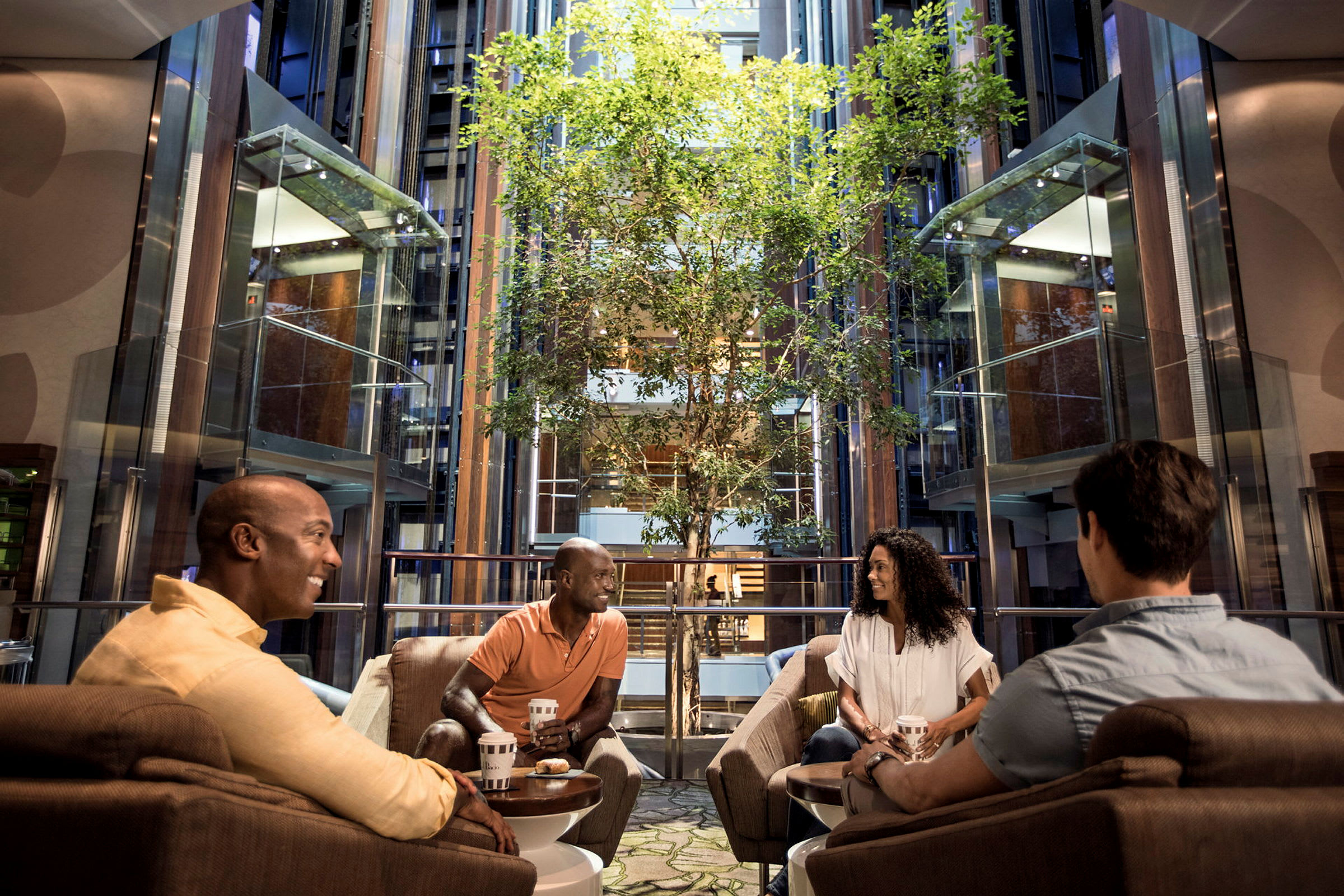 Personer sitter i en modern hotellobby med en trädtäppa och hissar. (AI-genererad text)