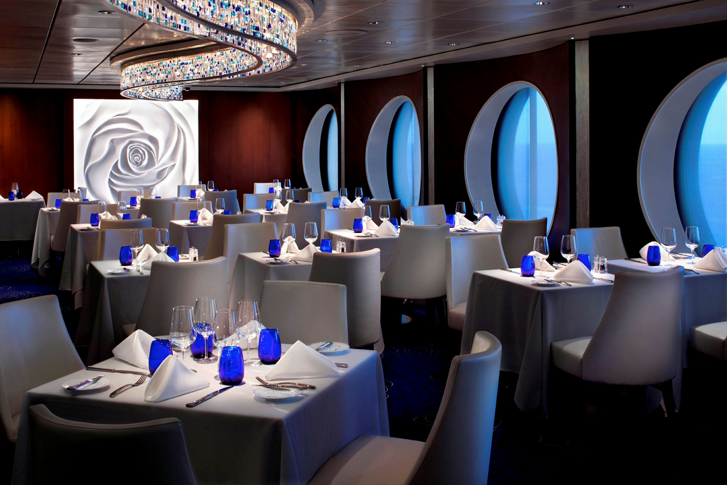 En elegant restaurang med dukade bord, blå glas och fönster med havsutsikt. (AI-genererad text)
