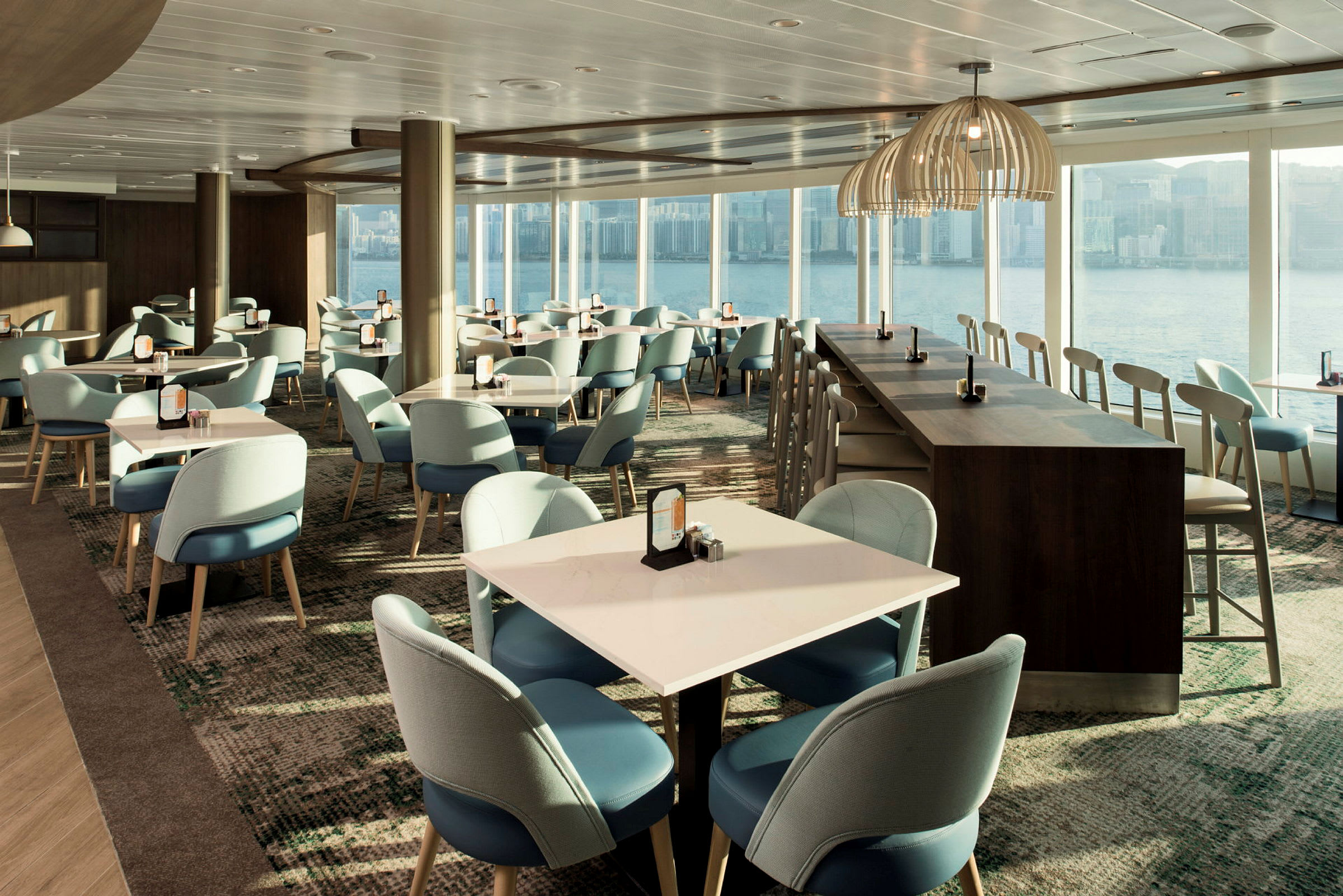 Interiör av en modern restaurang med bord och stolar samt utsikt över vatten genom stora fönster. (AI-genererad text)