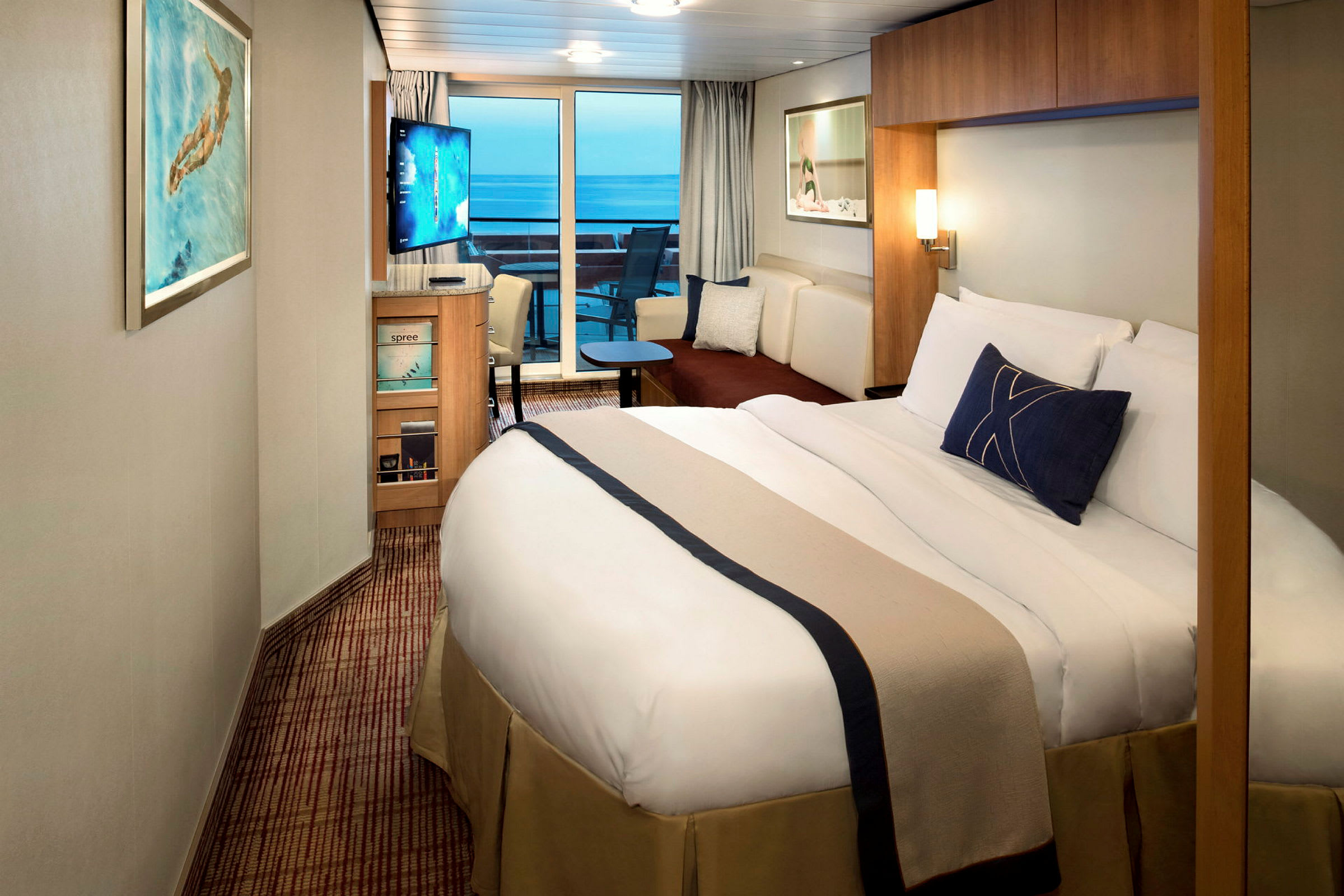 Ett hotellrum med en dubbelsäng, TV, soffa och glasdörrar som leder till en balkong med utsikt över havet. (AI-genererad text)