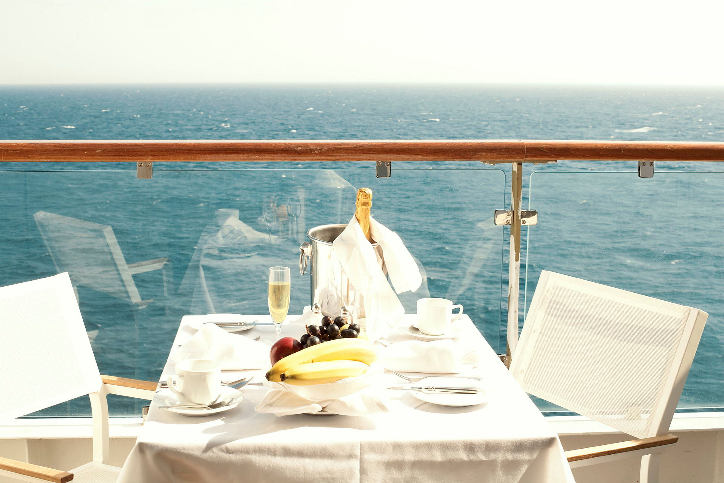 Ett dukat bord med frukter och champagne på en balkong vid havet. (AI-genererad text)
