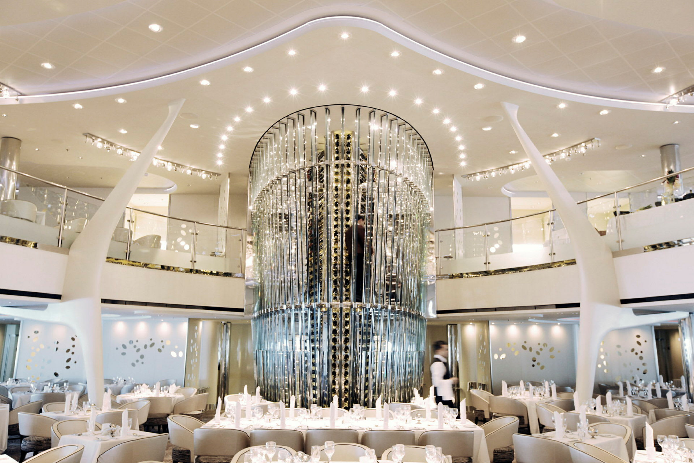 Interiör av en elegant restaurang med vita möbler och dekorationer samt ett stort glastorn i mitten. (AI-genererad text)