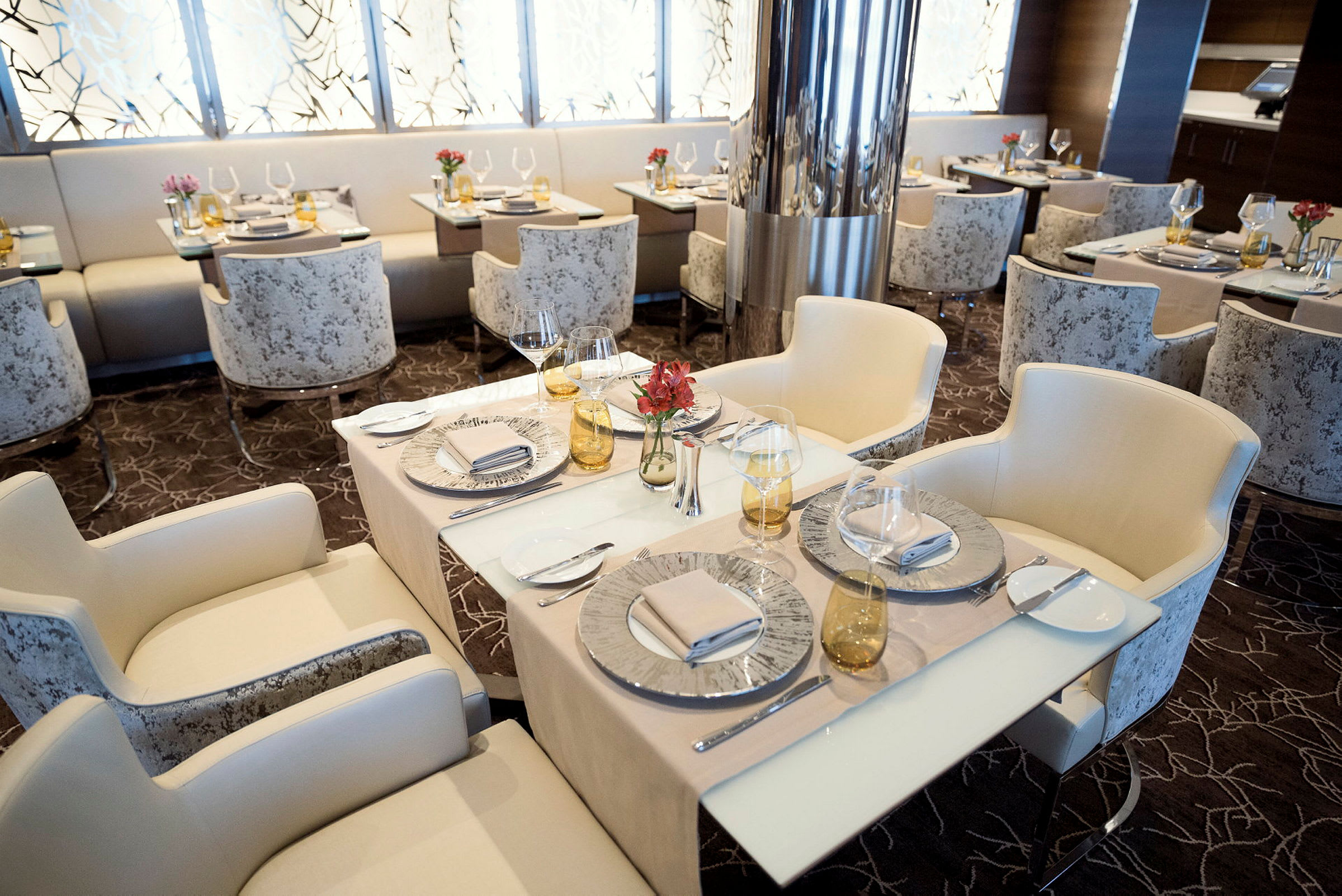 En elegant restaurang med bord uppdukade med porslin, glas och servetter. Stolarna är vita och rummet är inrett i en modern stil. (AI-genererad text)
