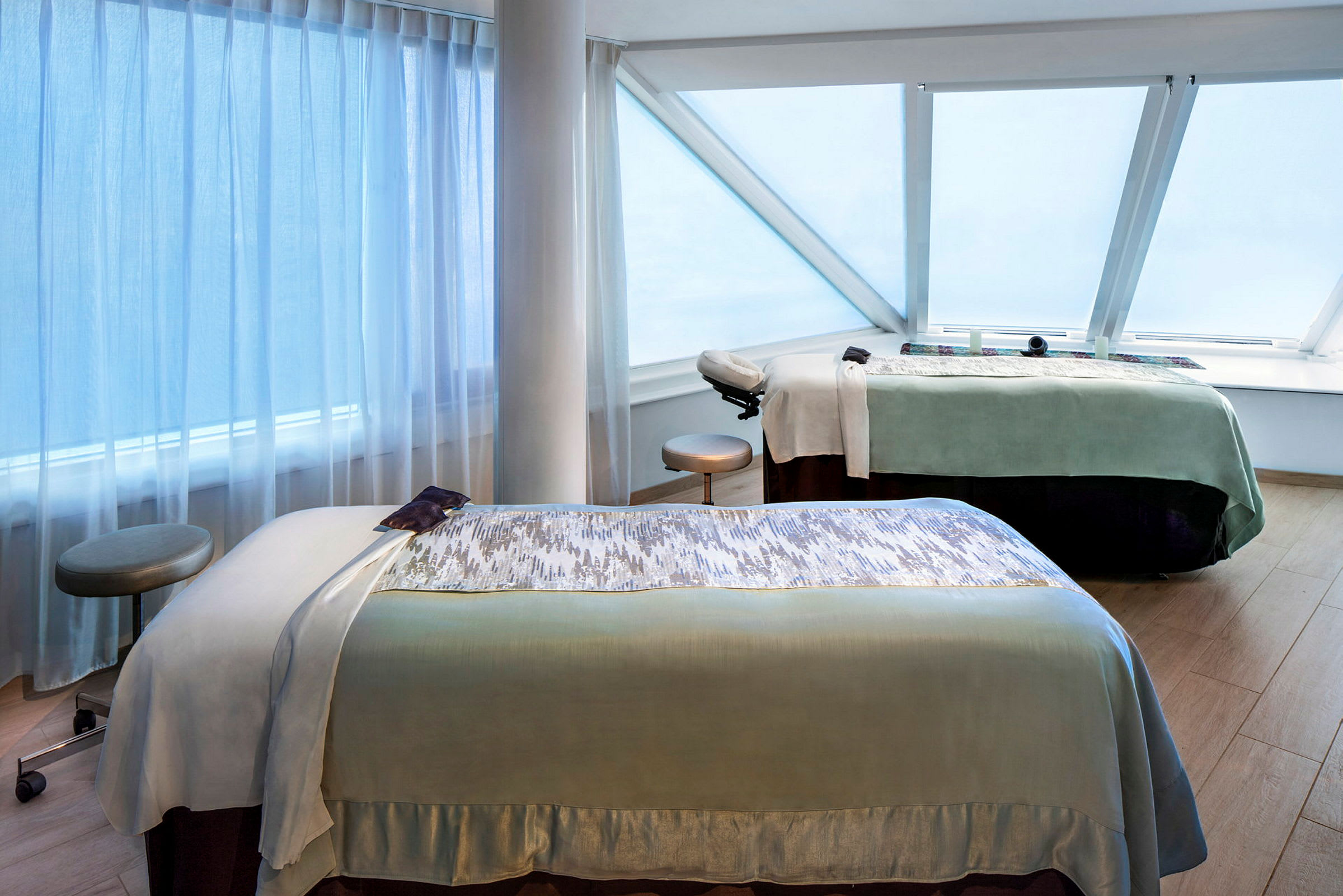 Två massagebänkar i ett rum med stora snedställda fönster. (AI-genererad text)