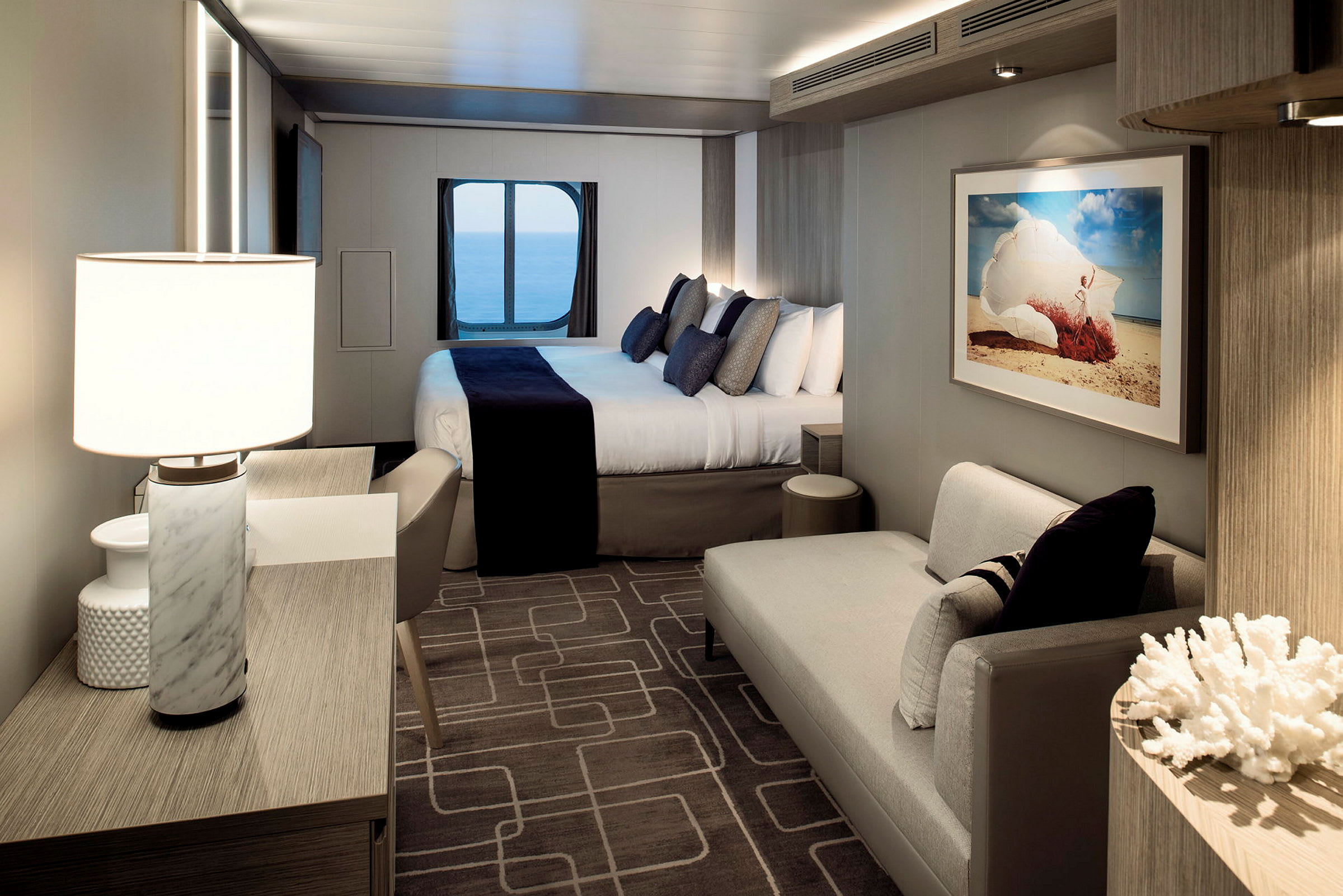 Modern och elegant hotellrum med en dubbelsäng, sittgrupp och sjöutsikt genom ett runt fönster. (AI-genererad text)