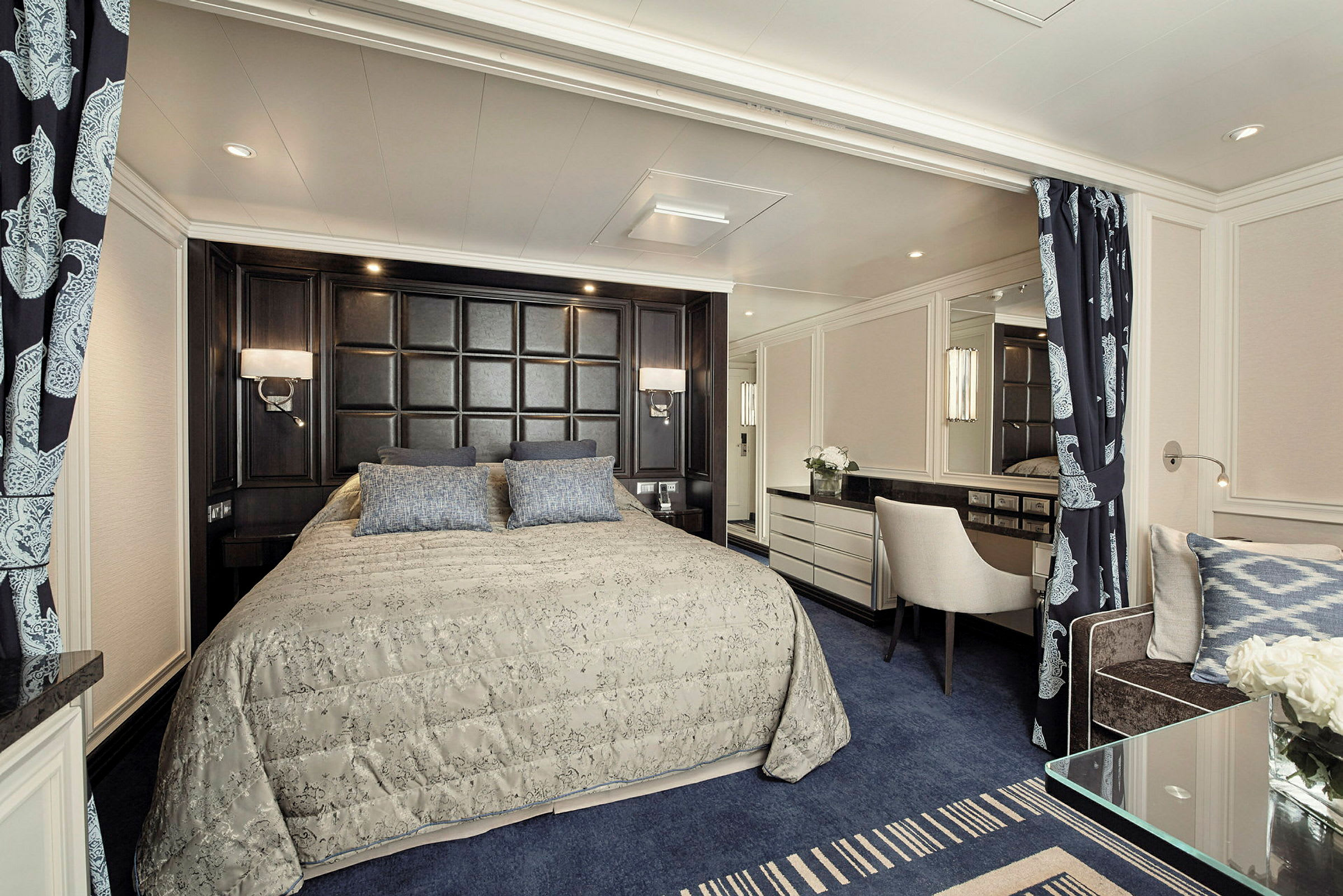 Ett elegant hotellrum med en stor säng, mörkt huvudgavel, ljus inredning och blå detaljer. (AI-genererad text)